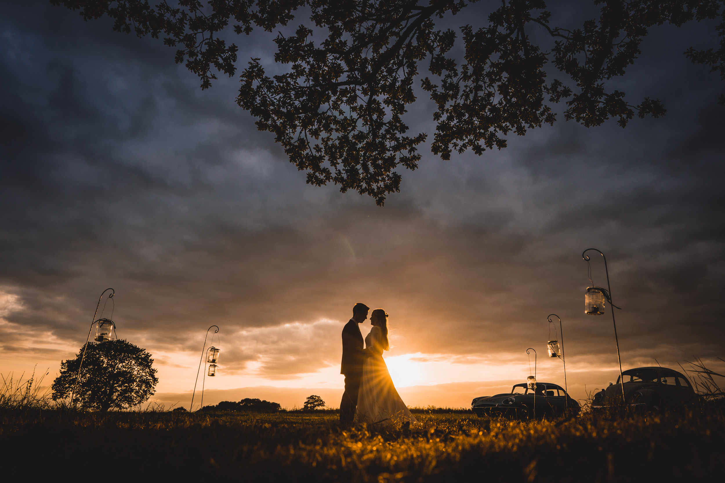 A bride and groom captured by a wedding photographer under a cloudy sky at sunset.