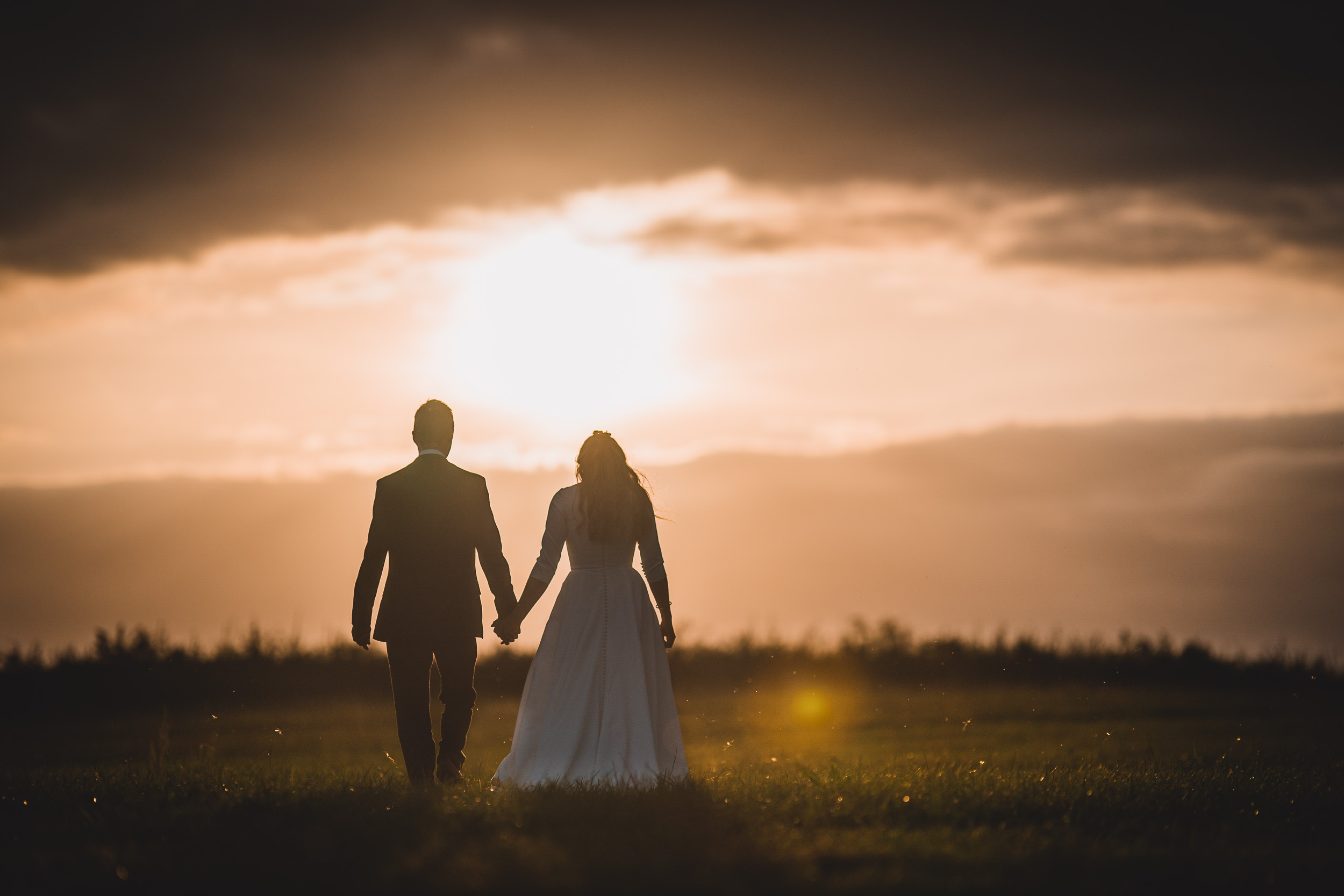 A stunning wedding photo of a bride and groom walking in a field at sunset, captured by a talented wedding photographer.