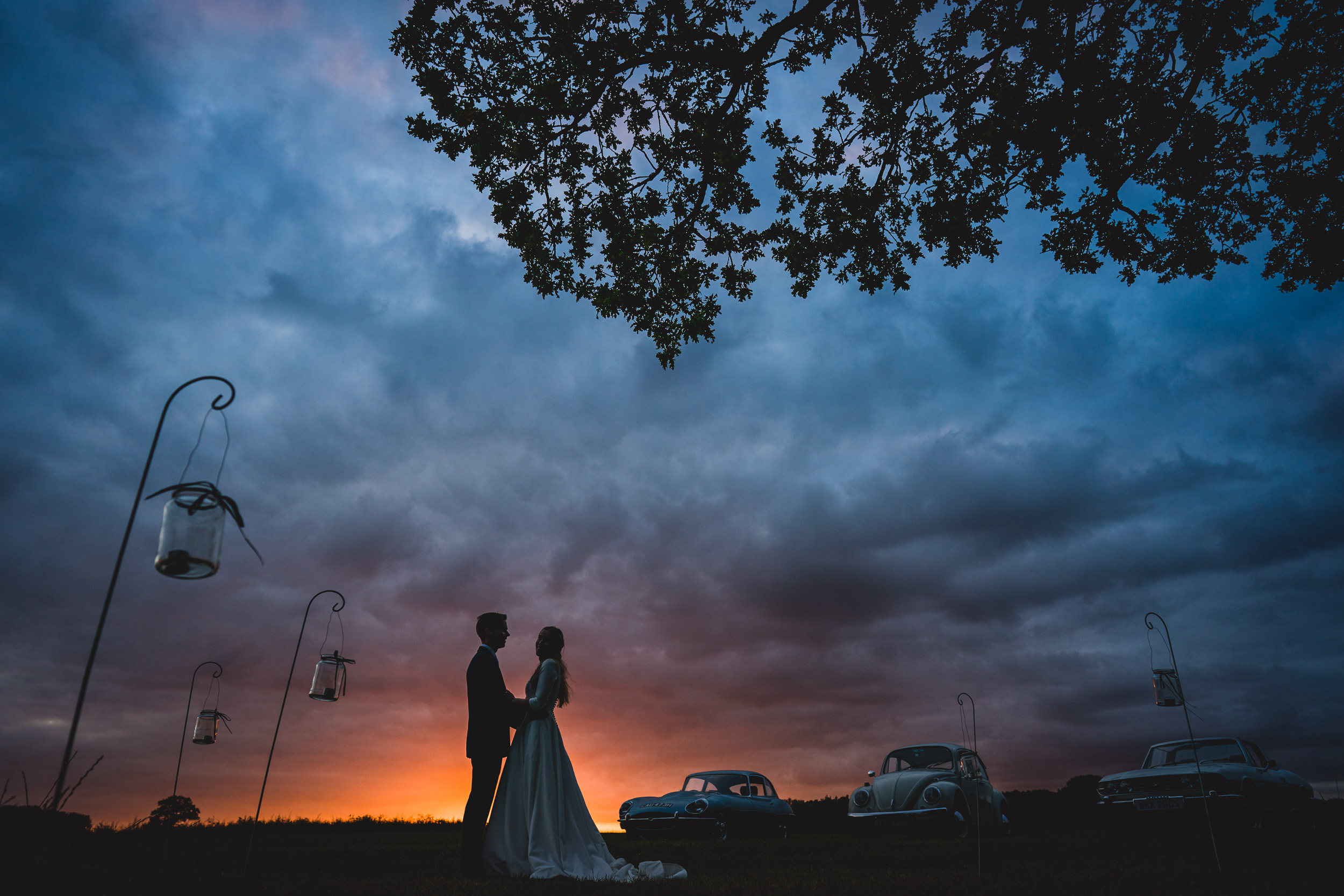 A wedding couple posed by a wedding photographer under a cloudy sky at sunset.