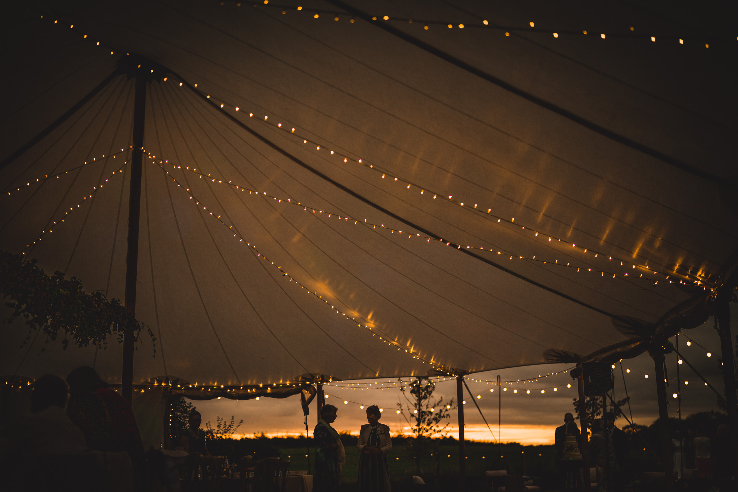 A wedding reception under a tent with string lights, celebrating the bride and groom.