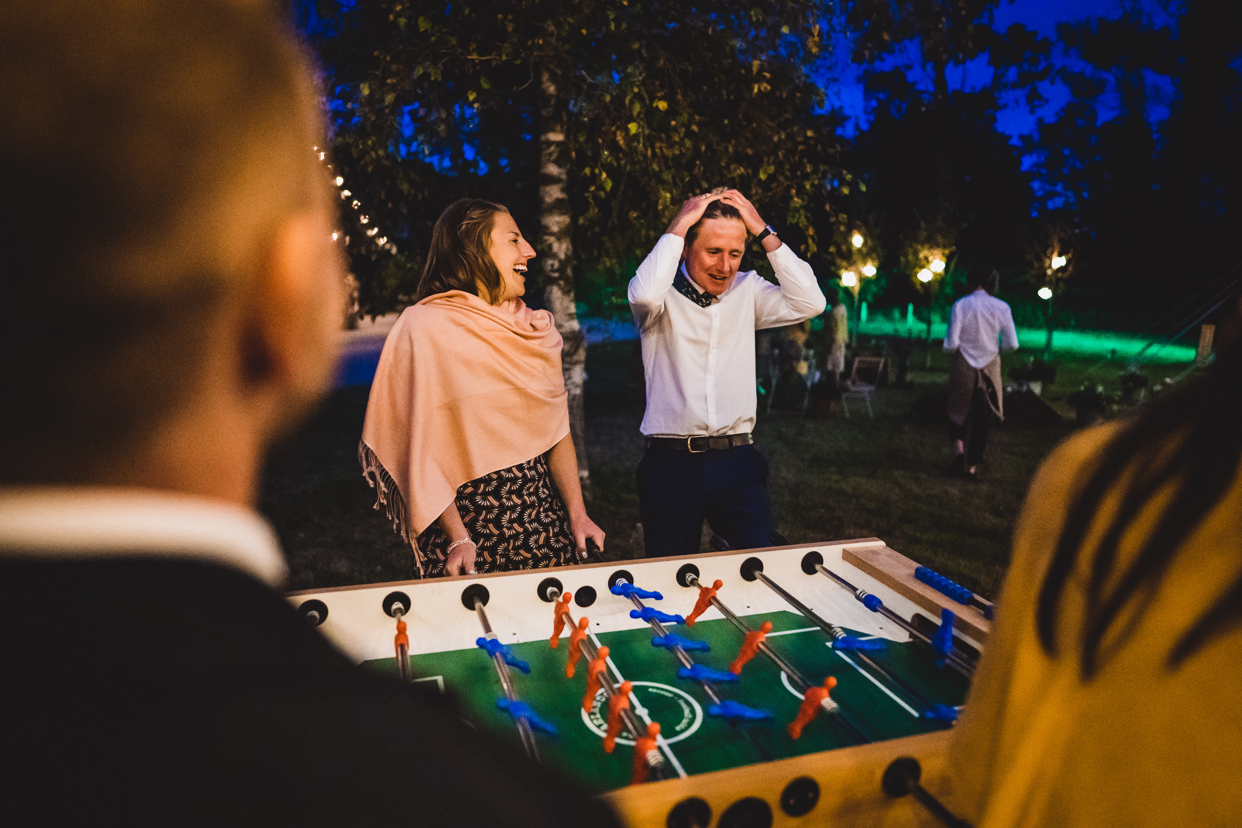 A bride and her wedding photographer capture a lively group playing foosball at the wedding.