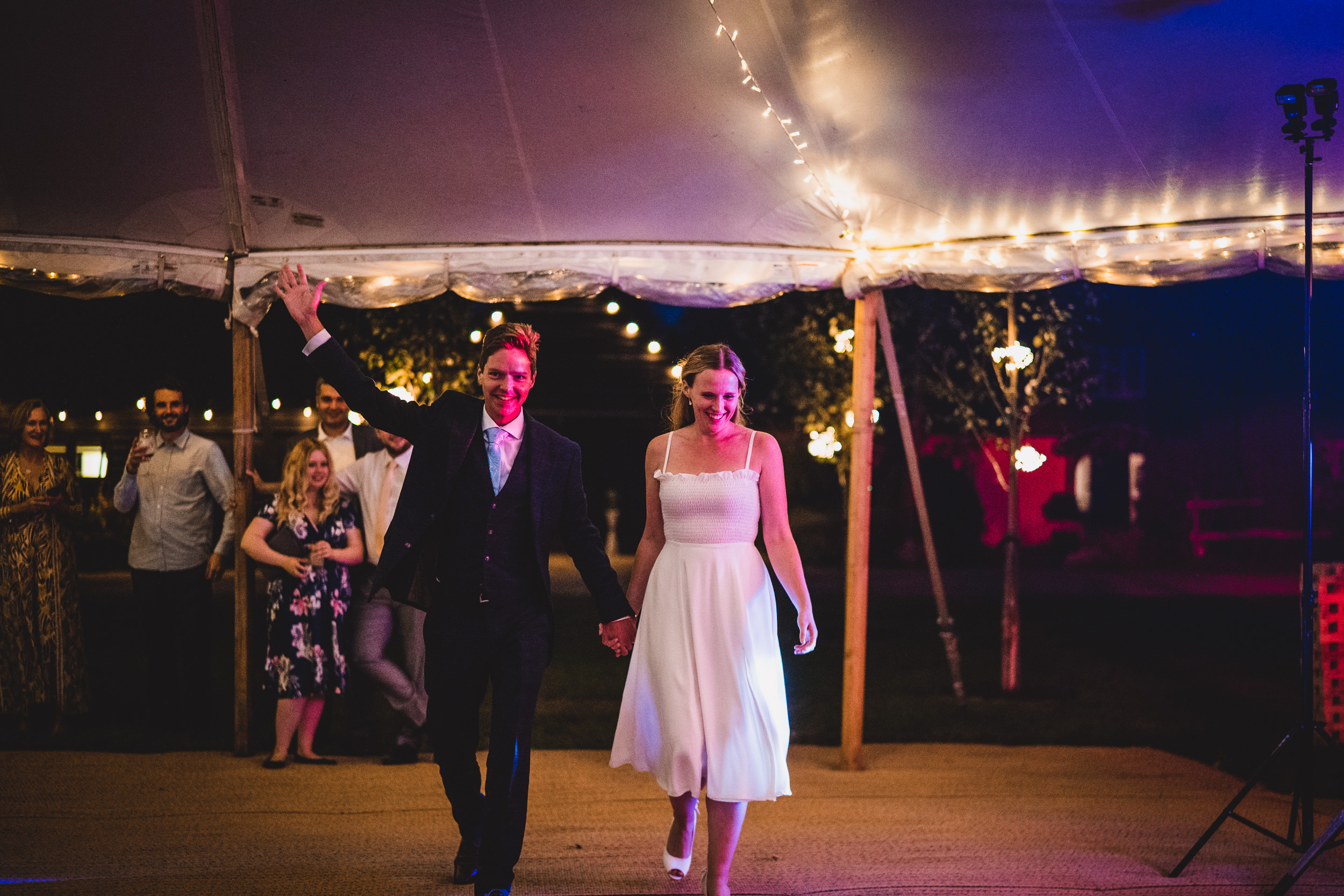 A wedding photographer captures a bride and groom walking down the aisle at their wedding reception.
