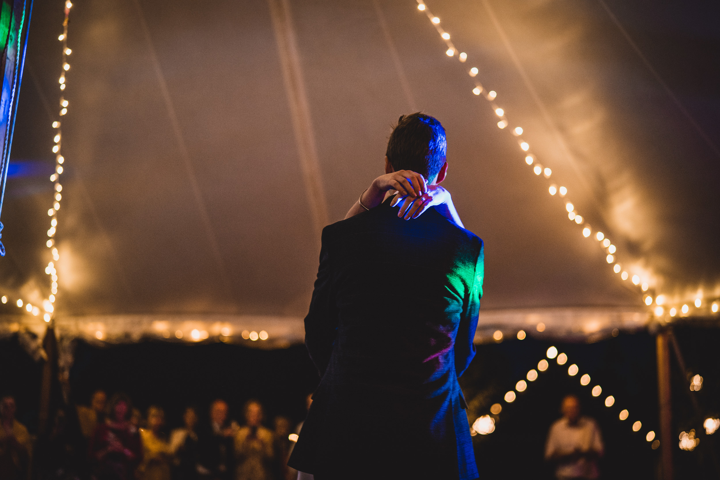 A wedding photographer captures a sweet moment of the groom embracing his bride inside a tent.