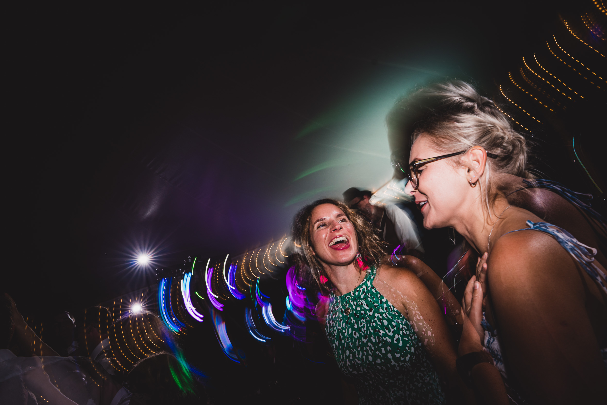 Two women, one as the bride, laughing with a wedding photographer at a party at night.