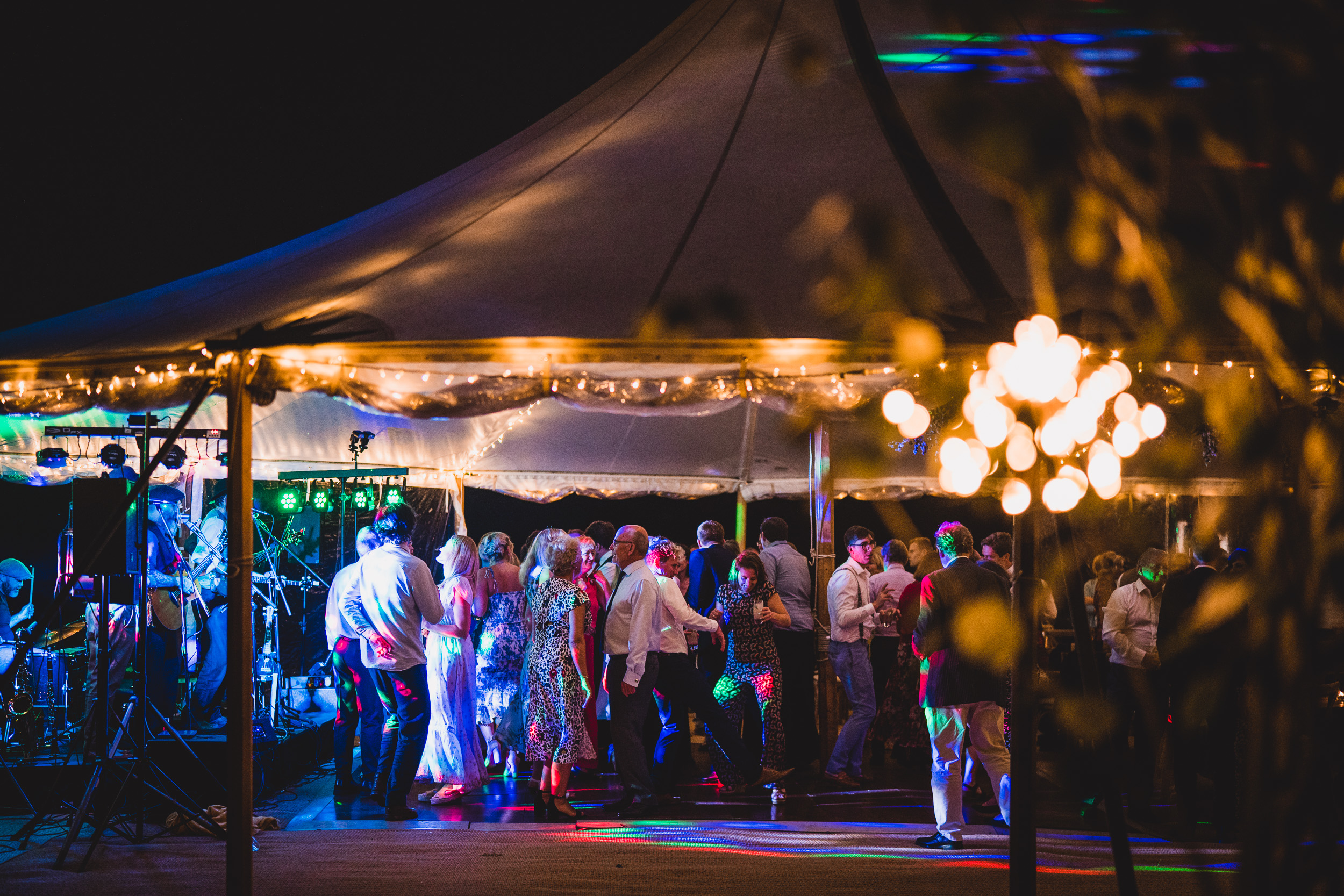 A groom and bride posing under a tent, captured by their wedding photographer at night.