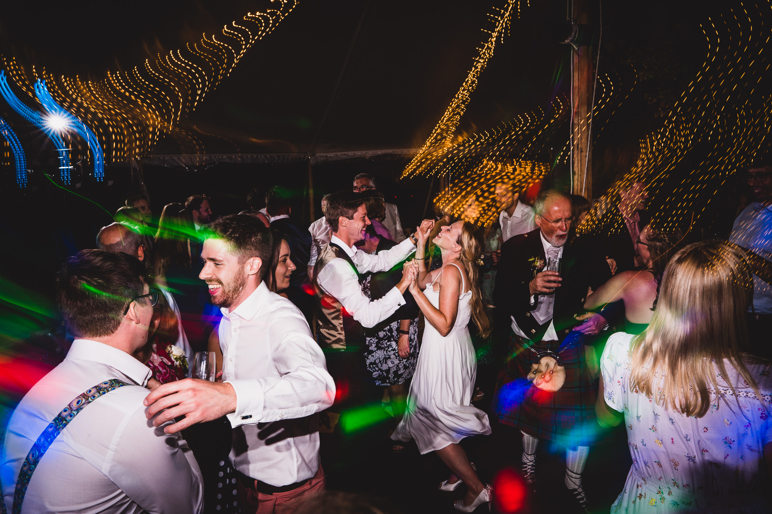 A bride and her wedding party dancing at a reception in a tent.