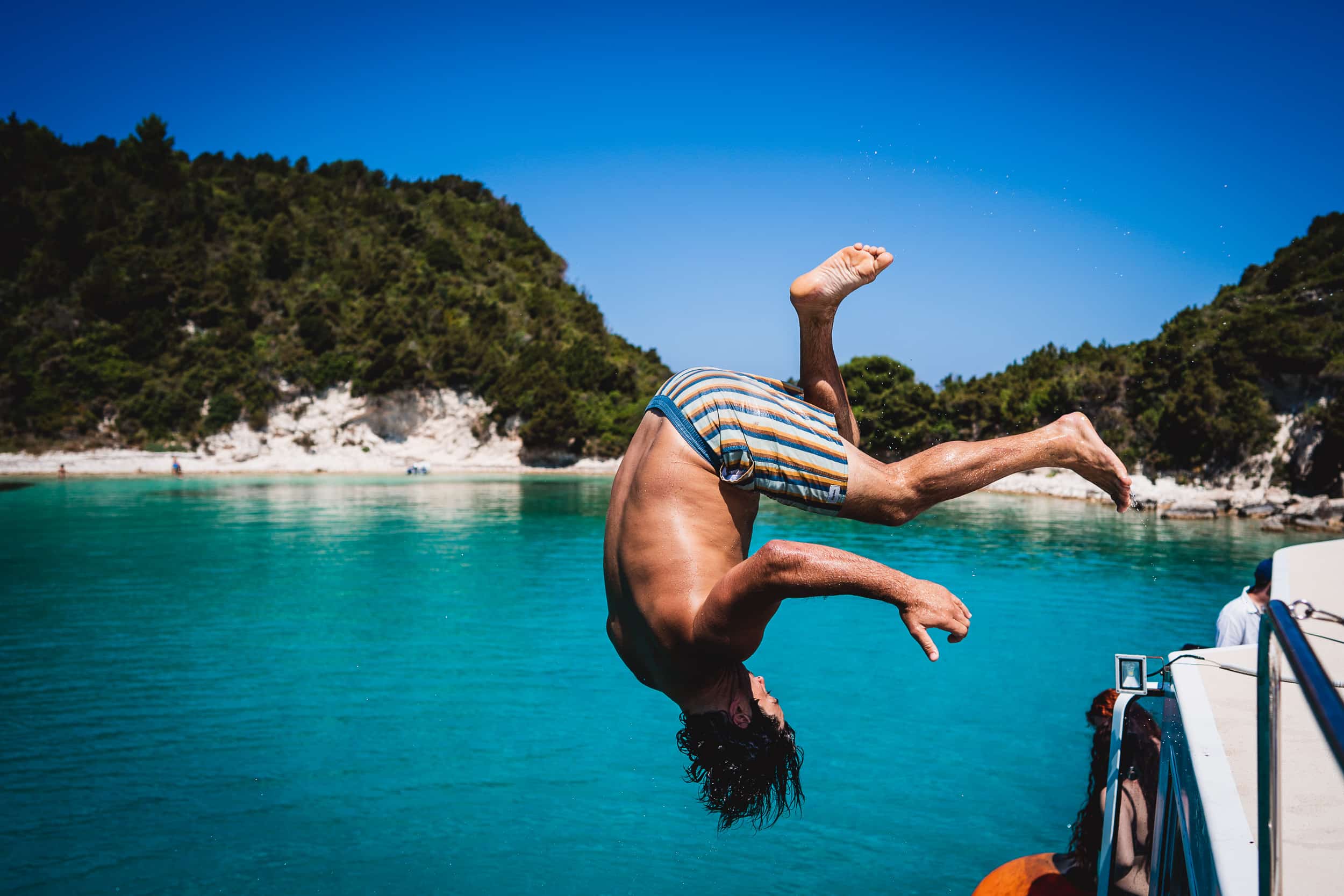 A groom captured by the wedding photographer as he leaps off a boat in a memorable wedding photo.