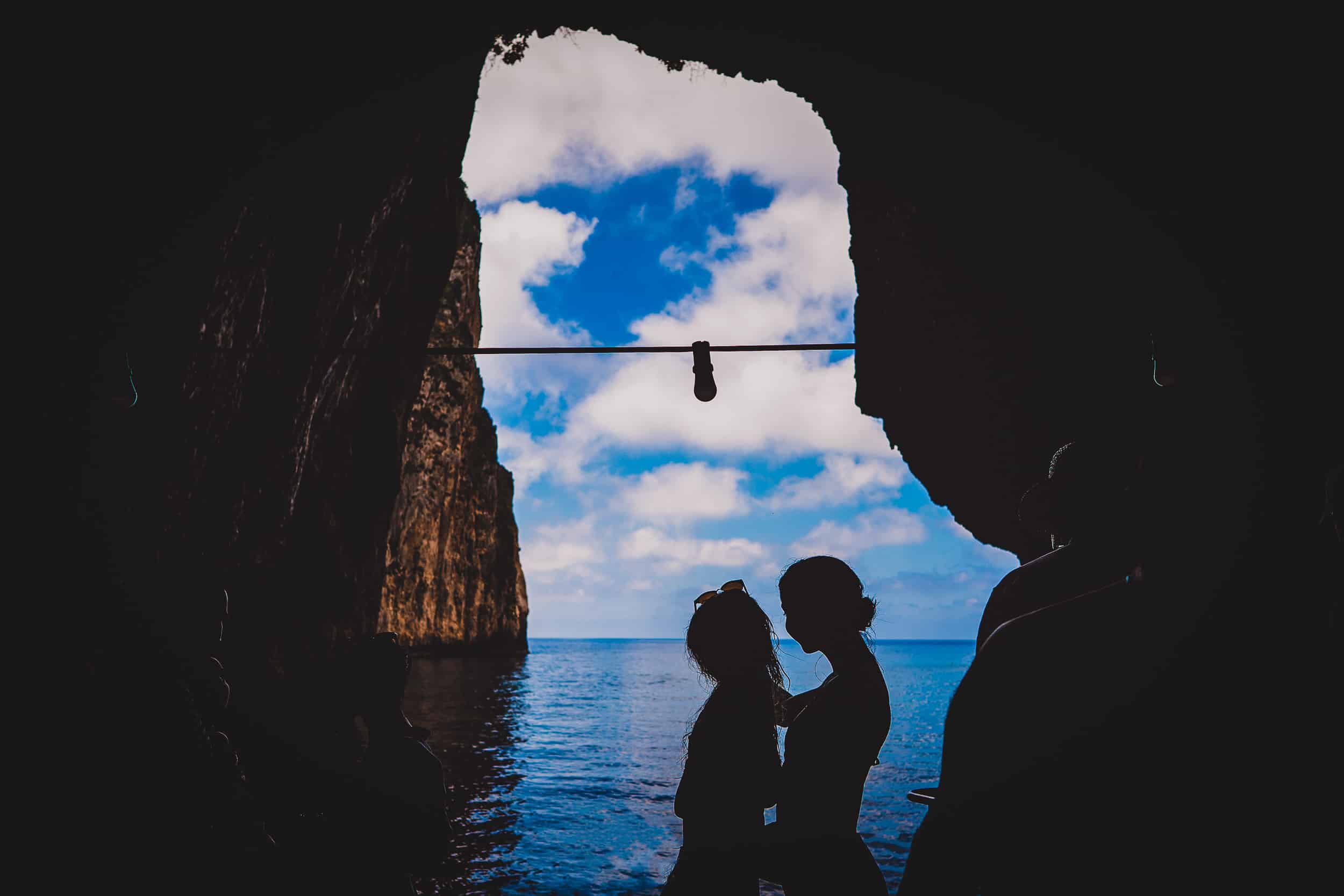 A wedding couple is silhouetted in a cave near the ocean, captured by a wedding photographer.