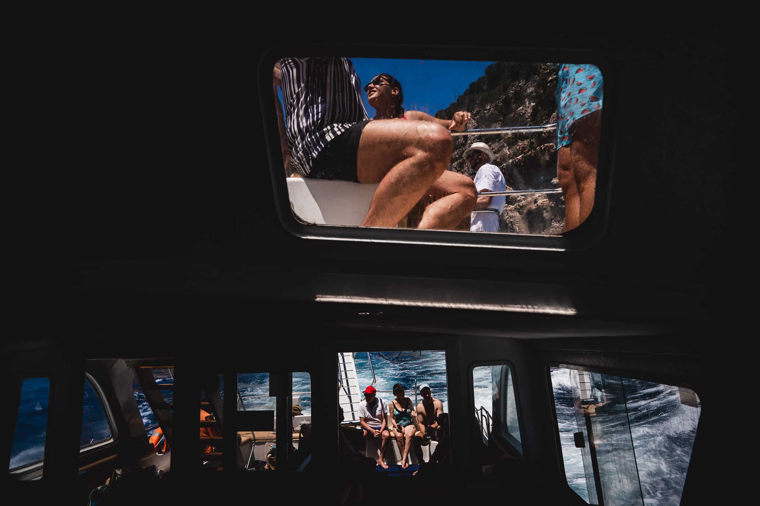 A group of people, including the bride, looking out of the window on a boat while posing for a wedding photo being taken by a wedding photographer.