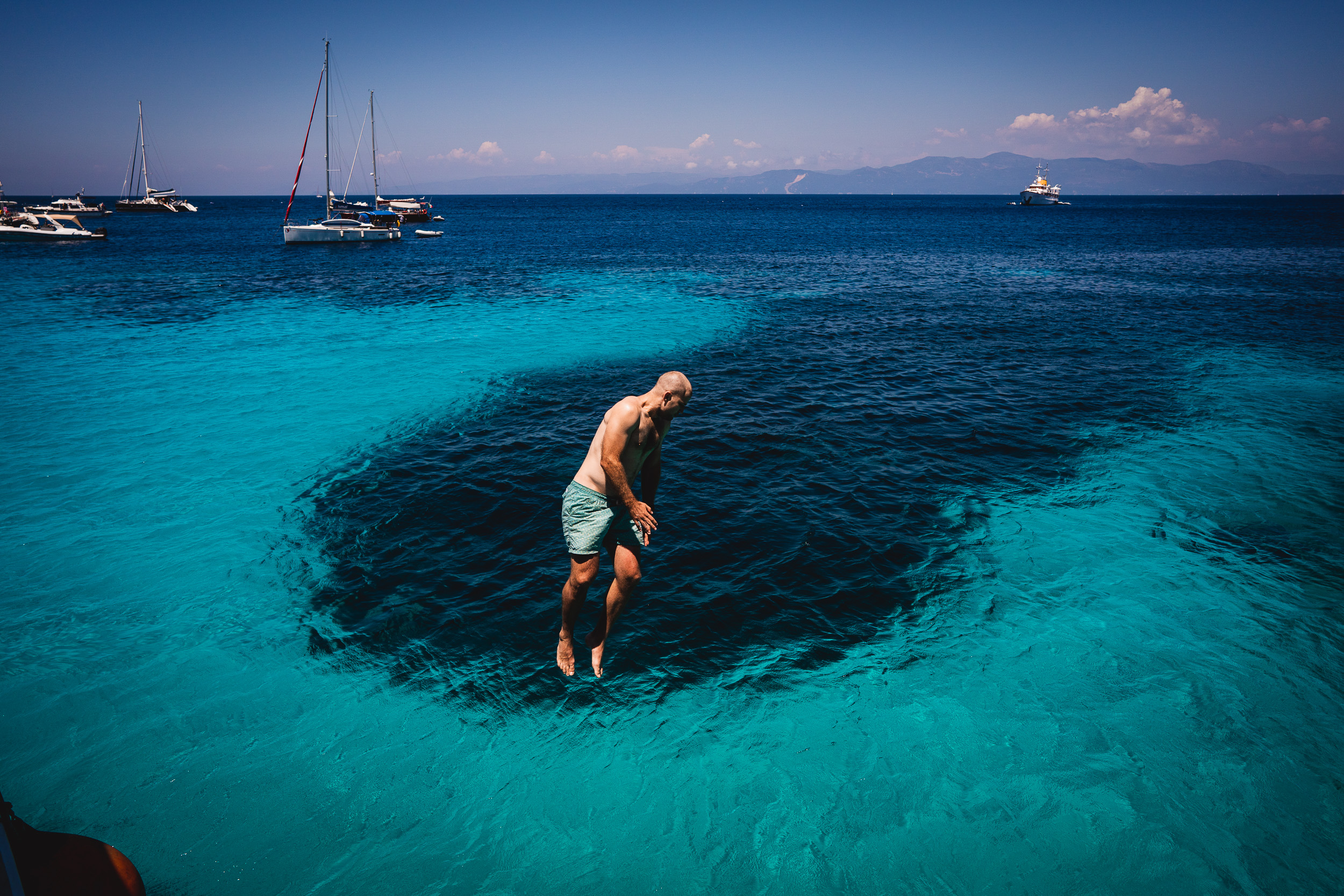 A groom is jumping into the water for a unique wedding photo.