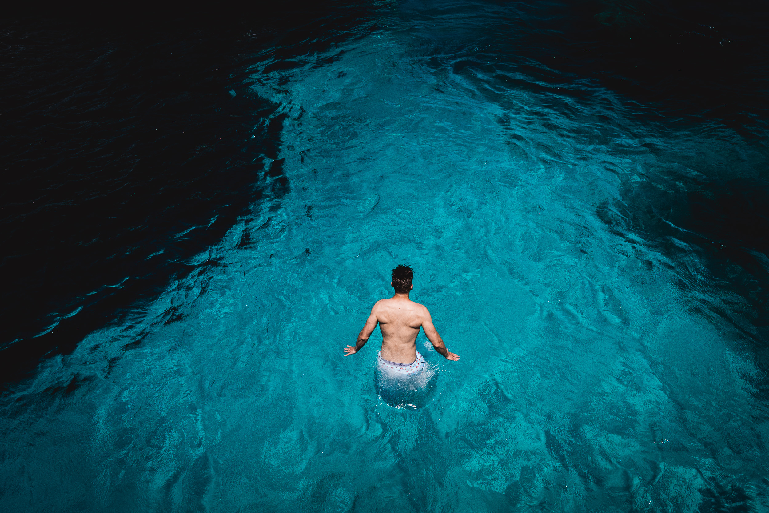 A groom standing in the water with his back to the camera.