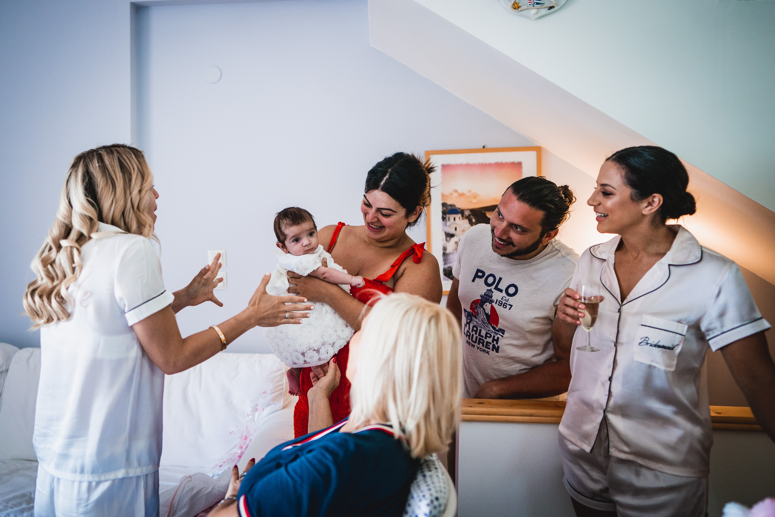 A group of people, including the groom and wedding photographer, standing around a baby in a room.