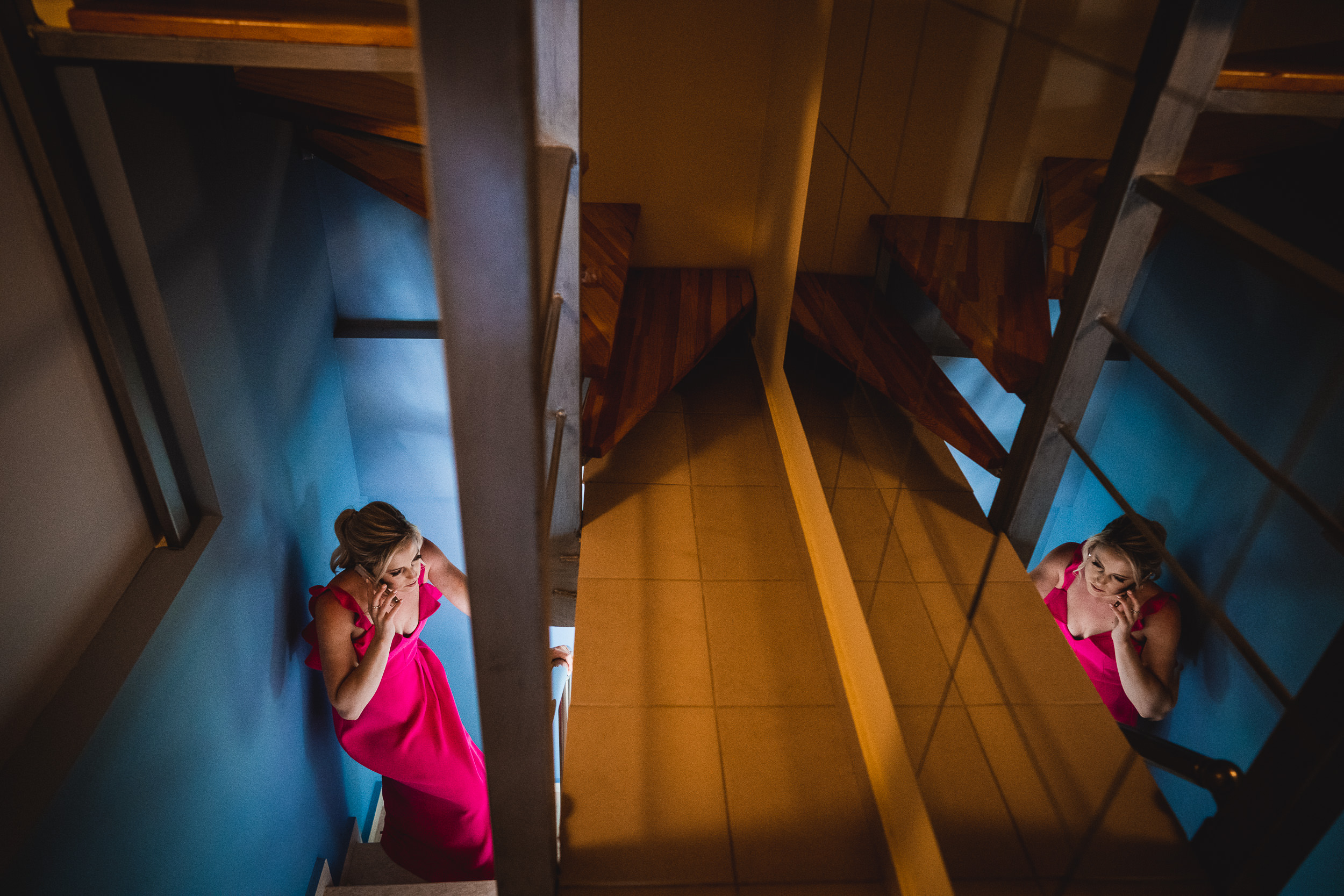 A woman in a pink dress poses on a staircase for a wedding photo.