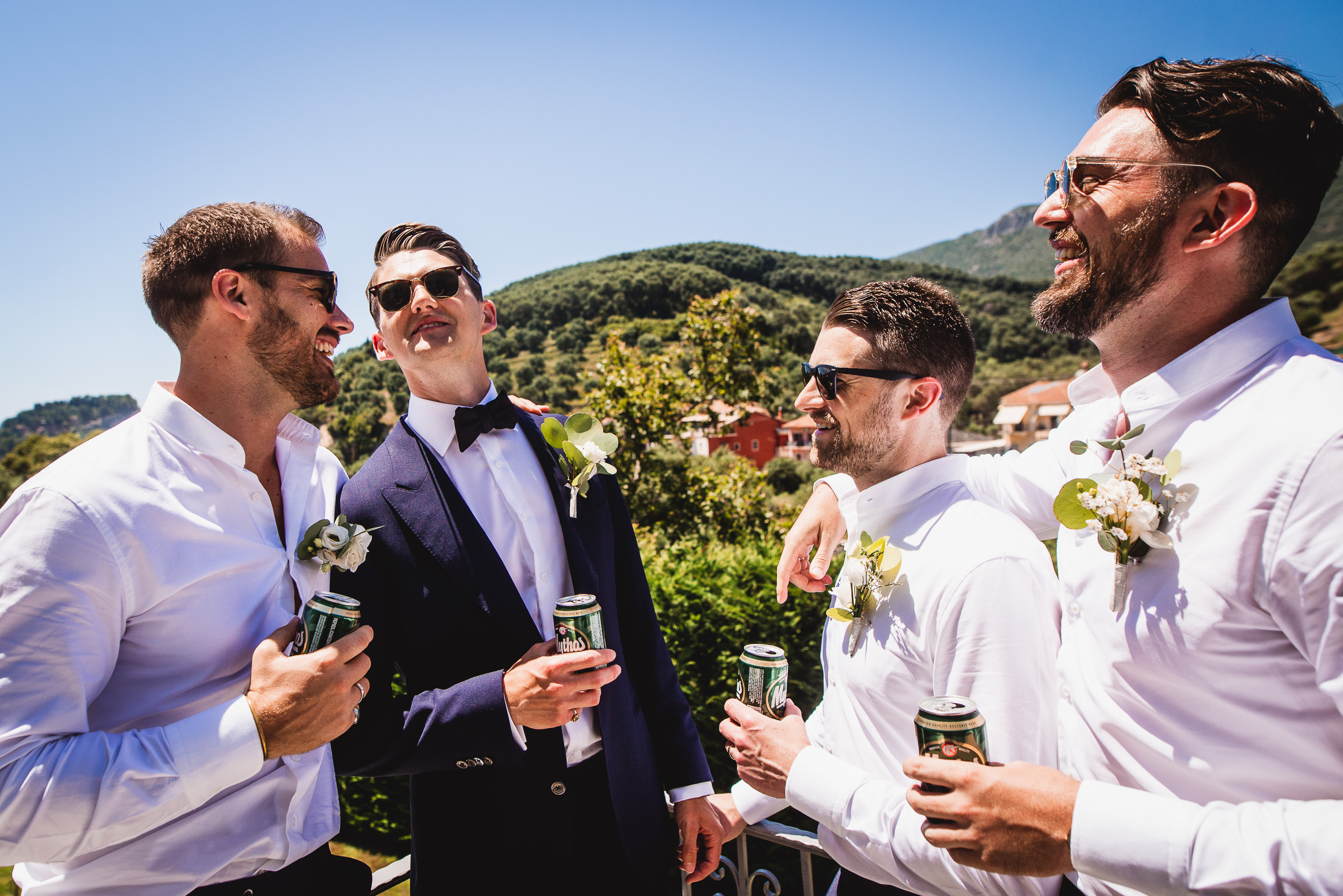 Groomsmen celebrating with beer on a balcony during a wedding.