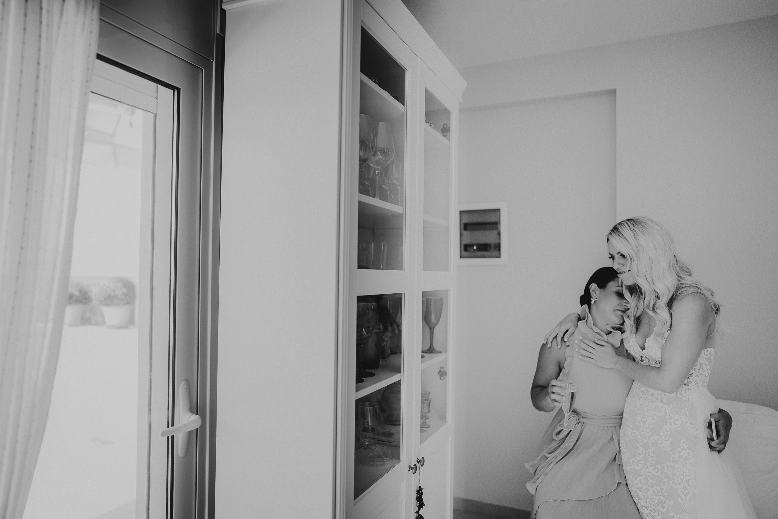 A bride is hugging her bridesmaid in a black and white wedding photo.
