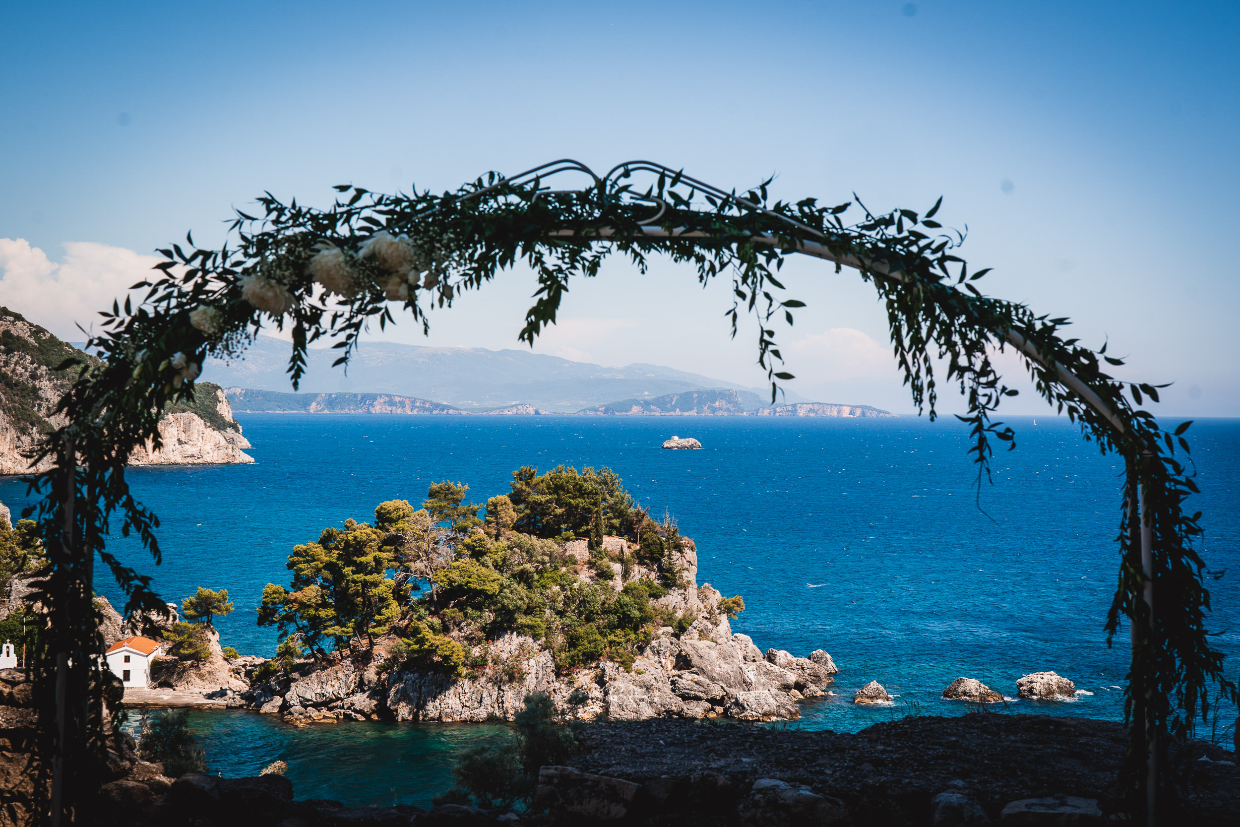 A bride posing for a wedding photo under a beautiful wedding arch overlooking the sea.