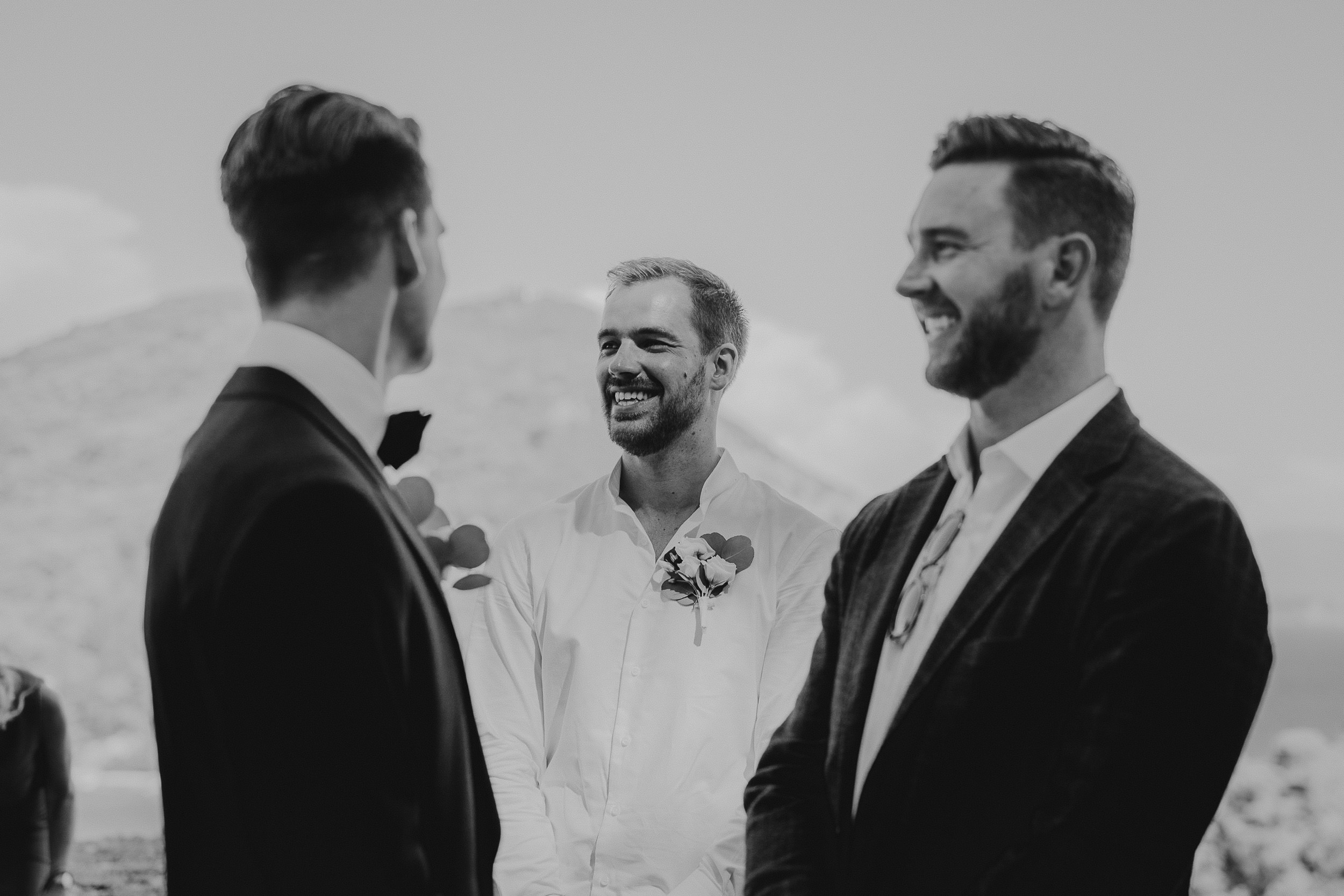 Groom and groomsmen smiling in black and white wedding photo.