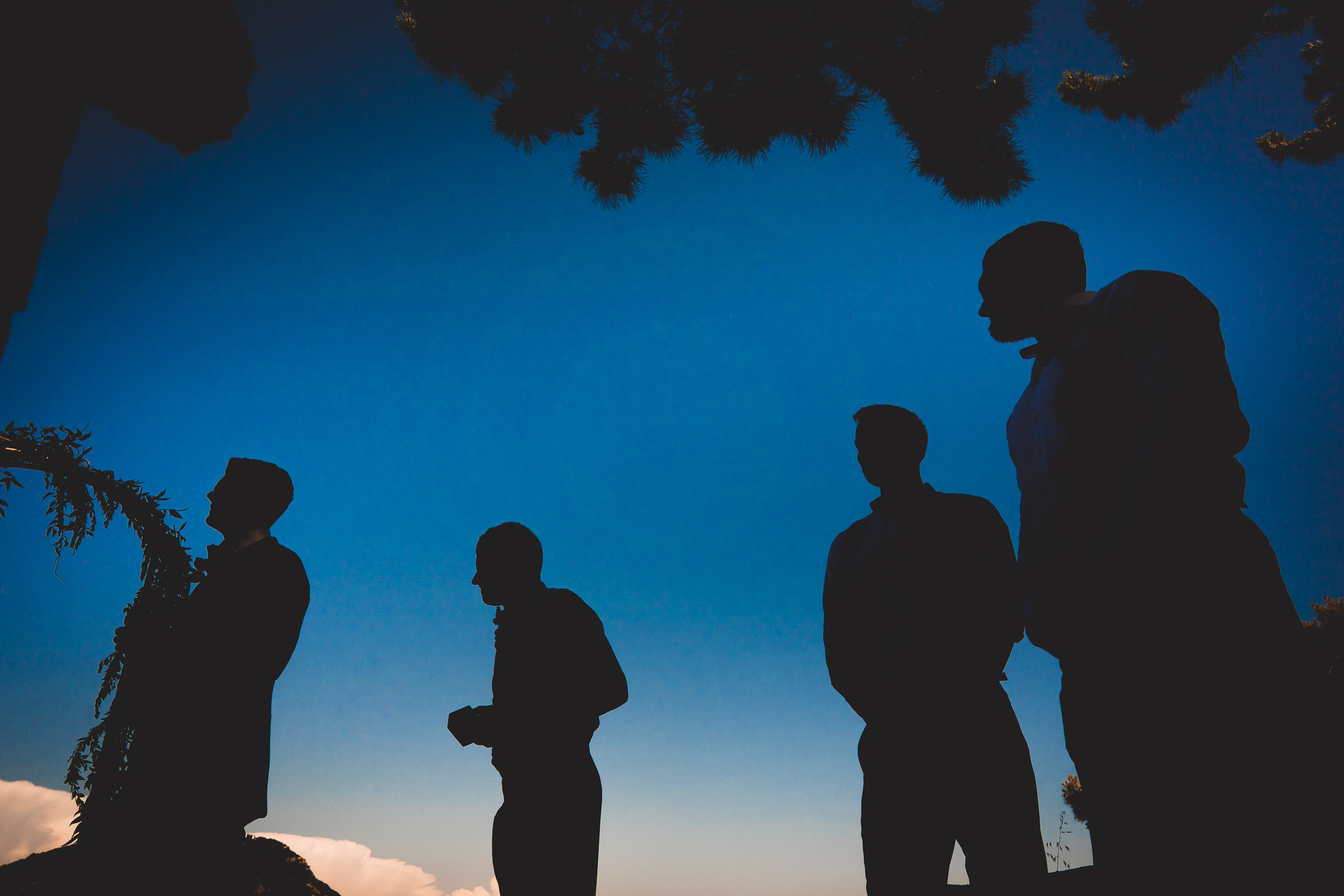 A group of men are silhouetted against a blue sky in a wedding photo.