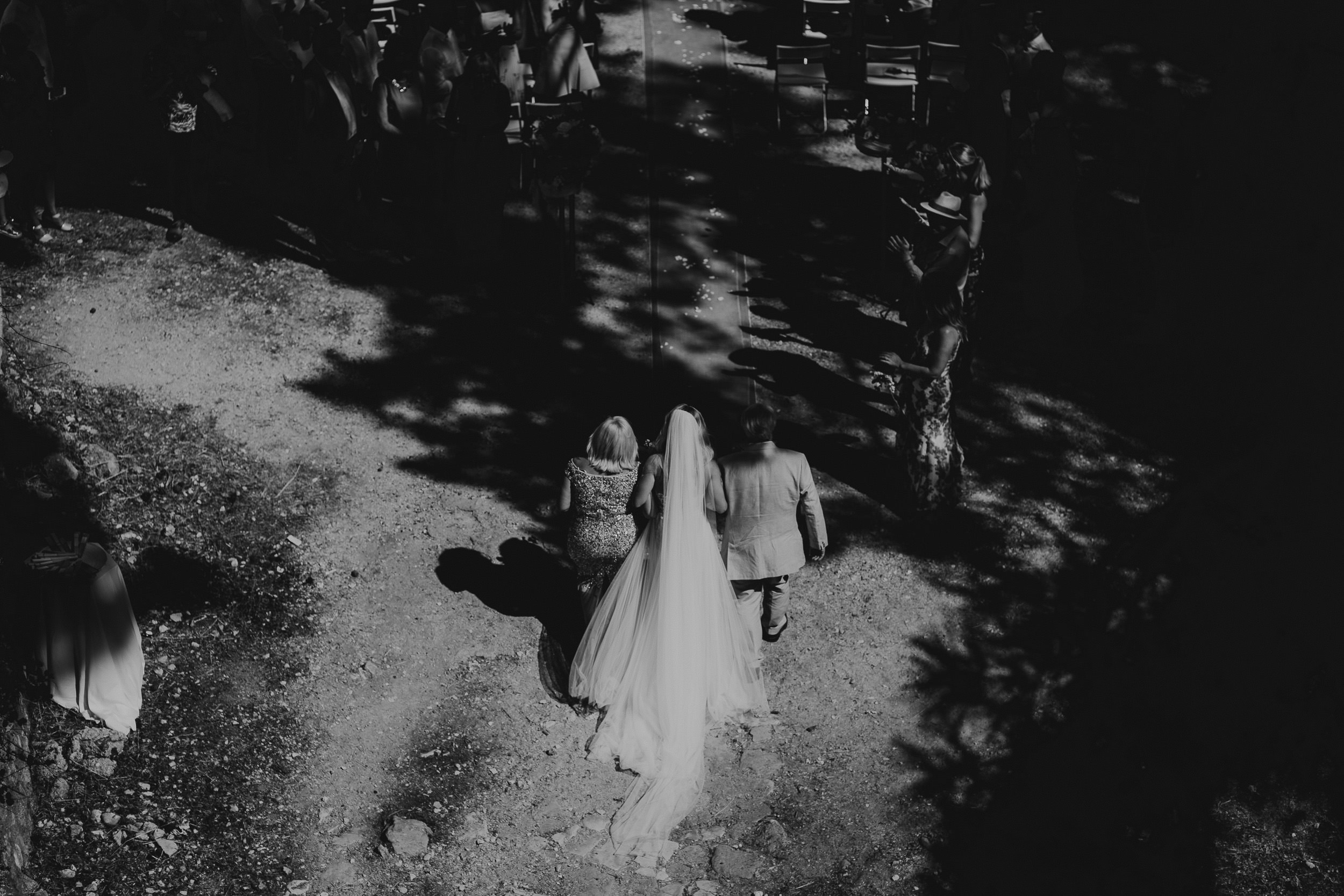 A wedding photographer captures a black and white photo of two brides walking down a path.