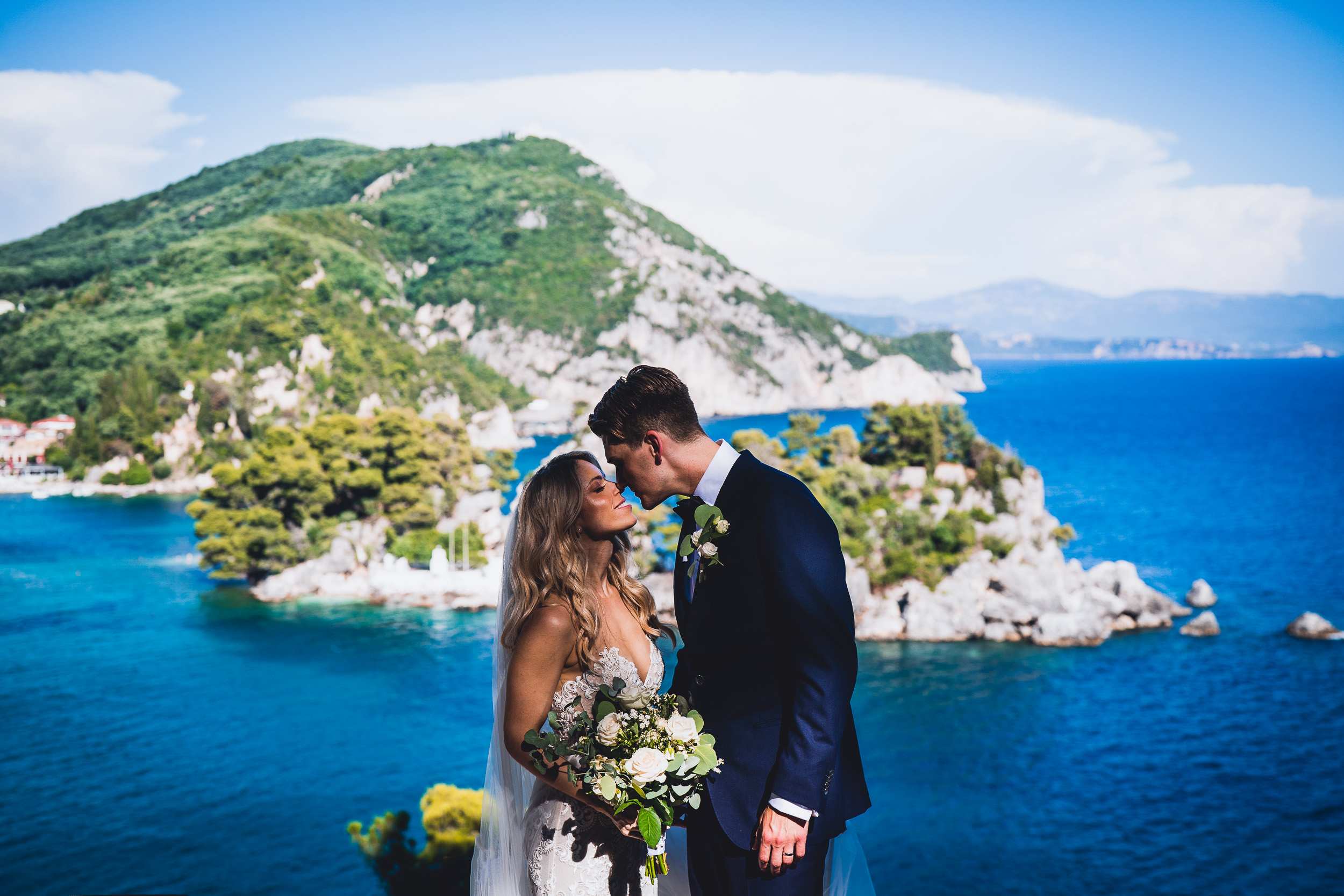 A wedding photo capturing a groom and bride sharing a kiss on a cliff overlooking the sea.