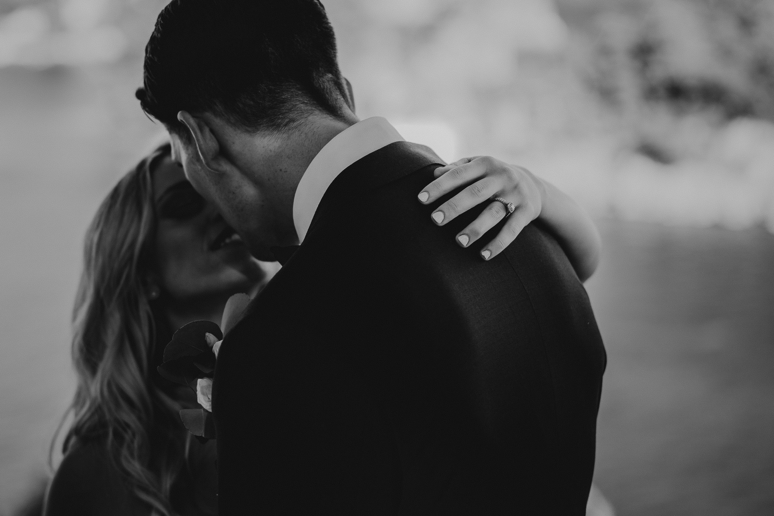 A wedding photographer captures a groom hugging his bride beside a lake.