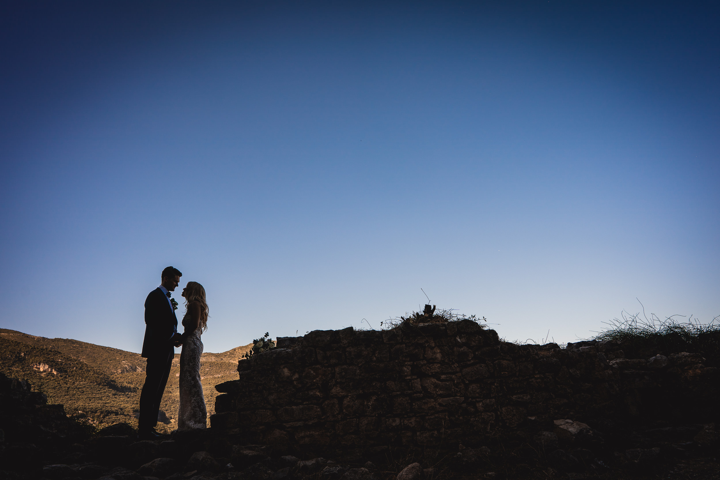 A wedding couple posing for their wedding photographer amidst ruins at sunset.