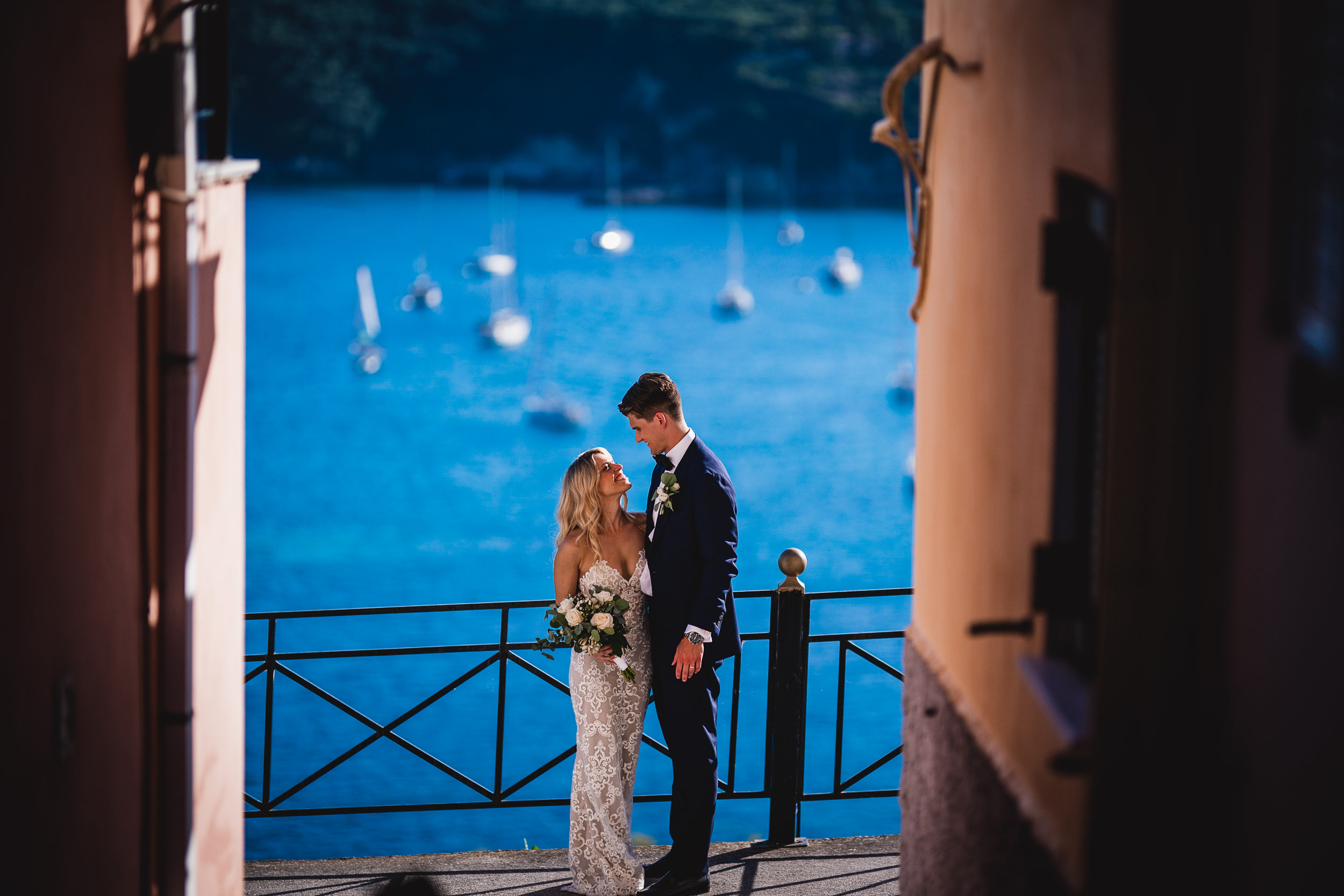 A wedding photographer capturing a bride and groom in an alleyway with boats in the background.