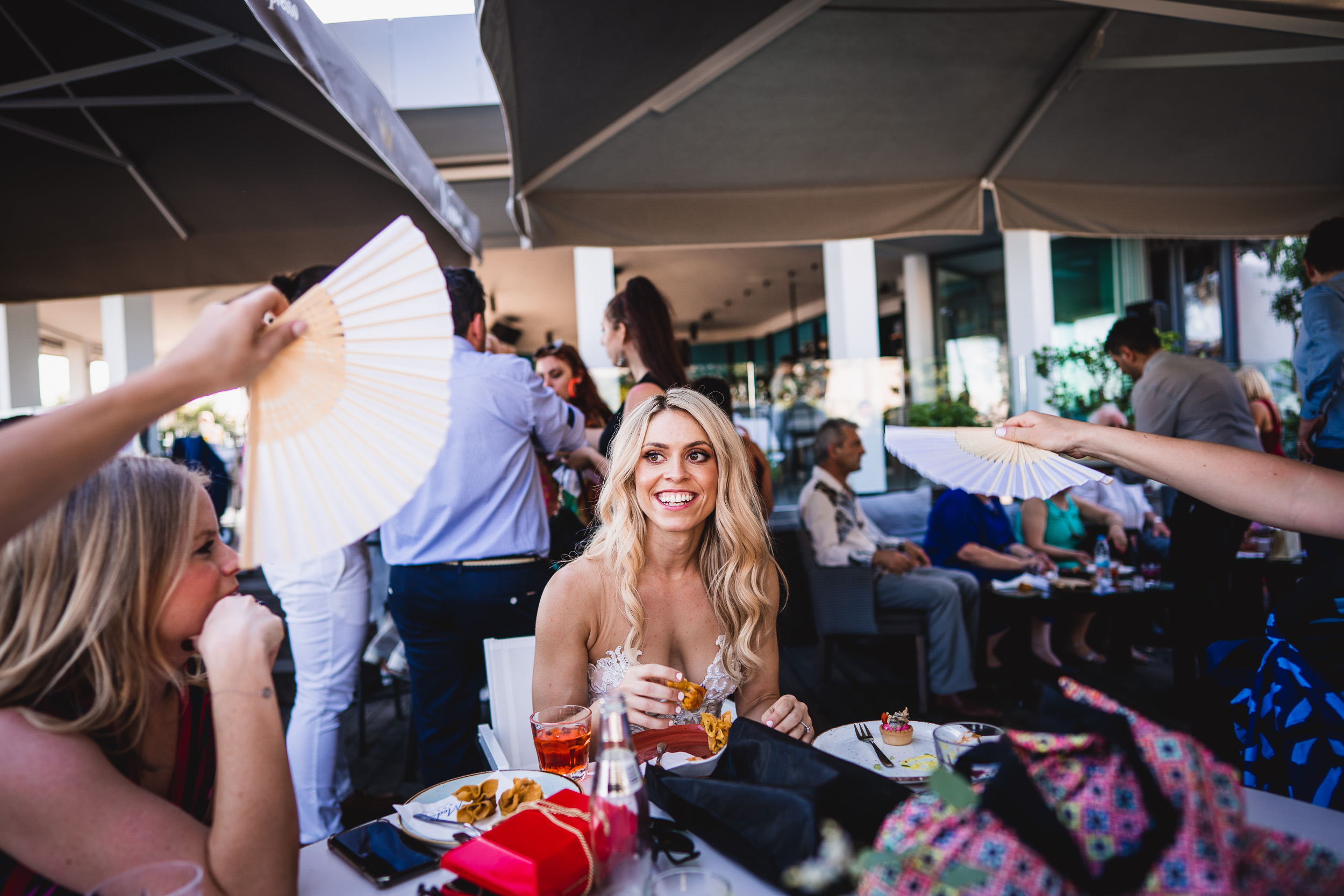 A wedding photographer captures a woman posing with a fan at a table during the wedding.