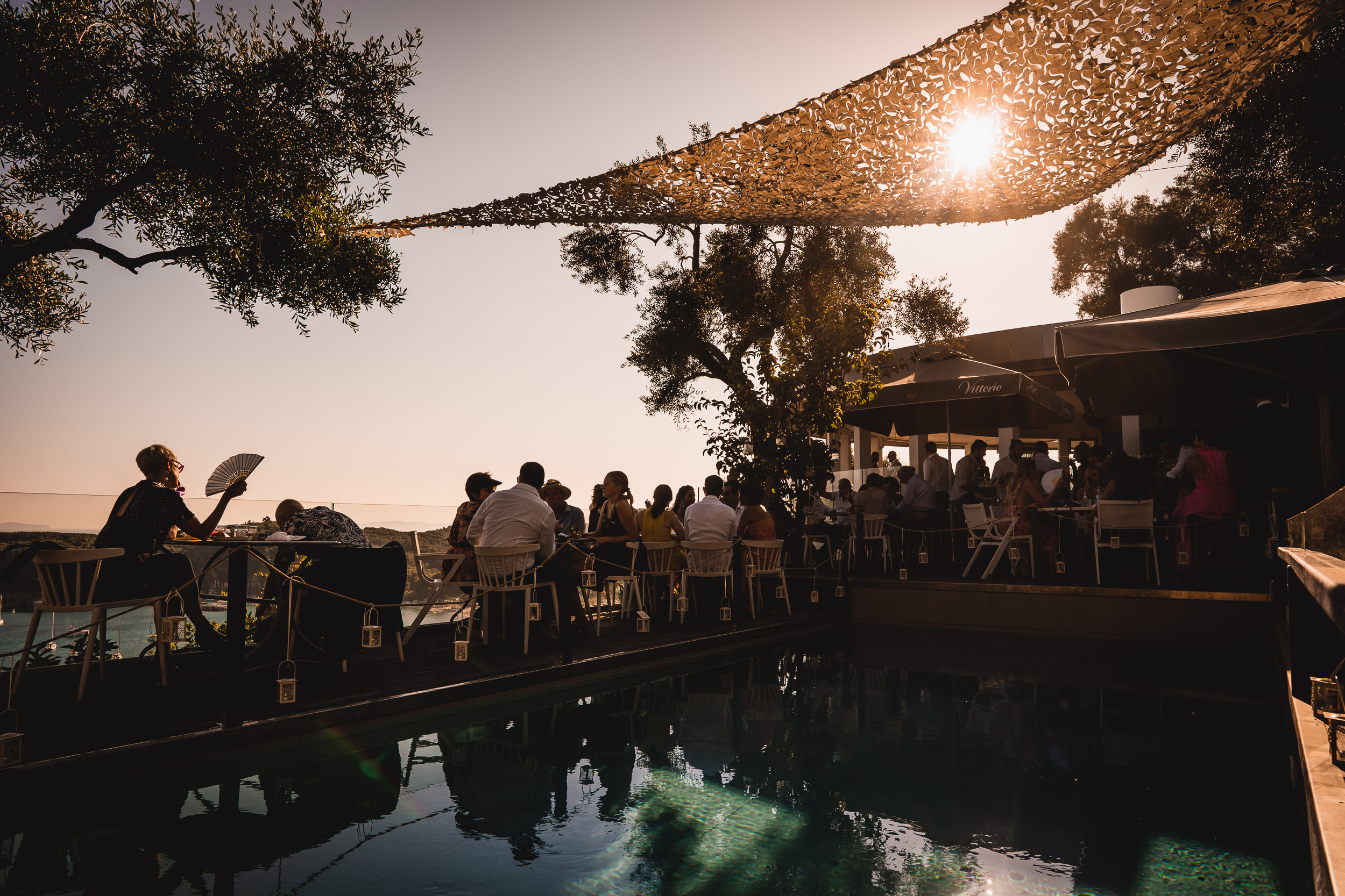 A group of people sitting around a pool at sunset, celebrating the groom's wedding.