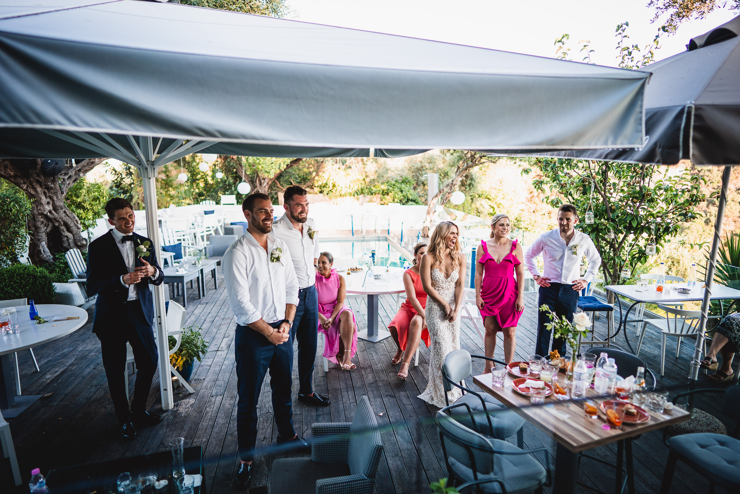 A group of people, including the groom and wedding photographer, standing under a tent at a wedding.