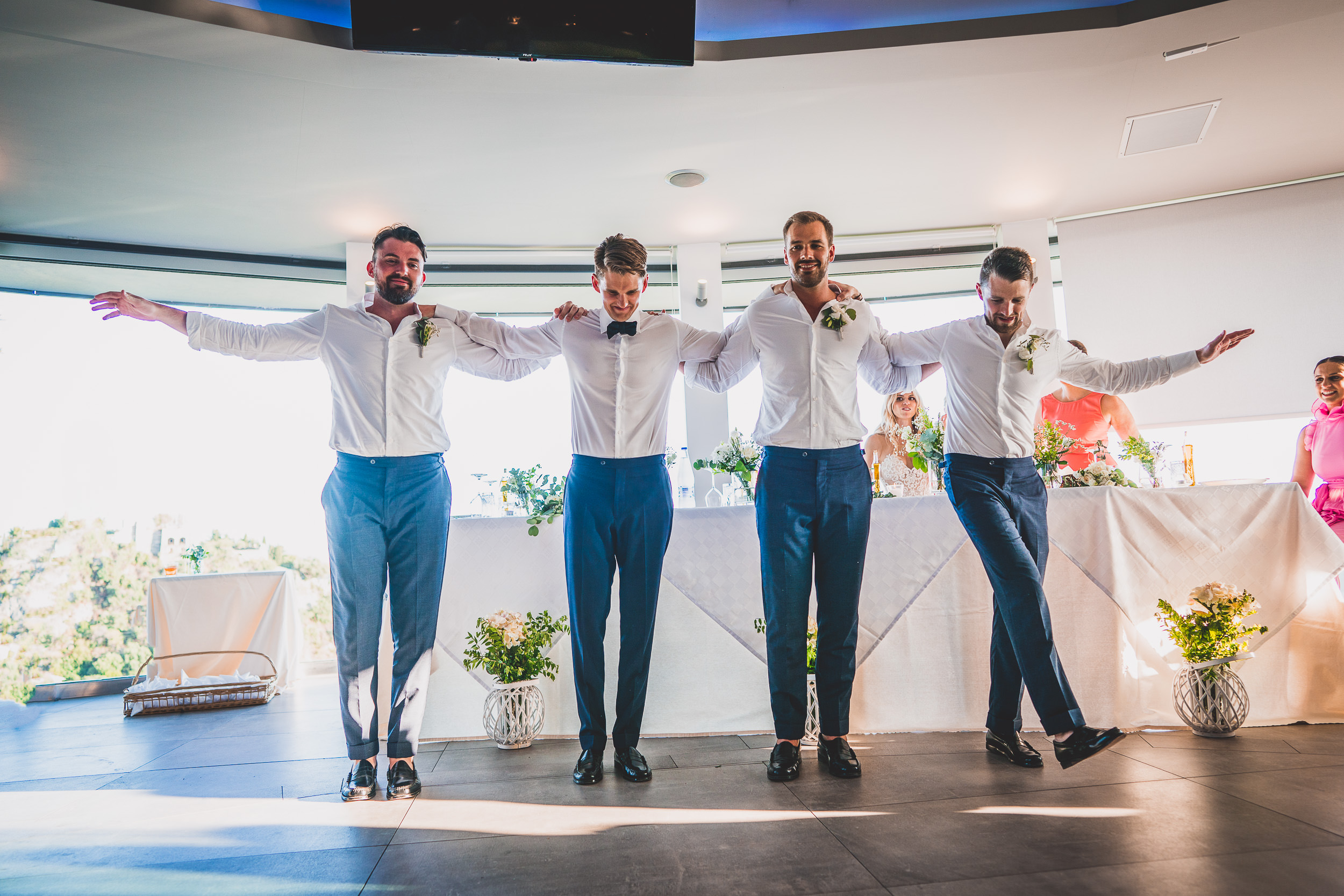 A group of groomsmen posing for a wedding photo in front of the bride and a table.