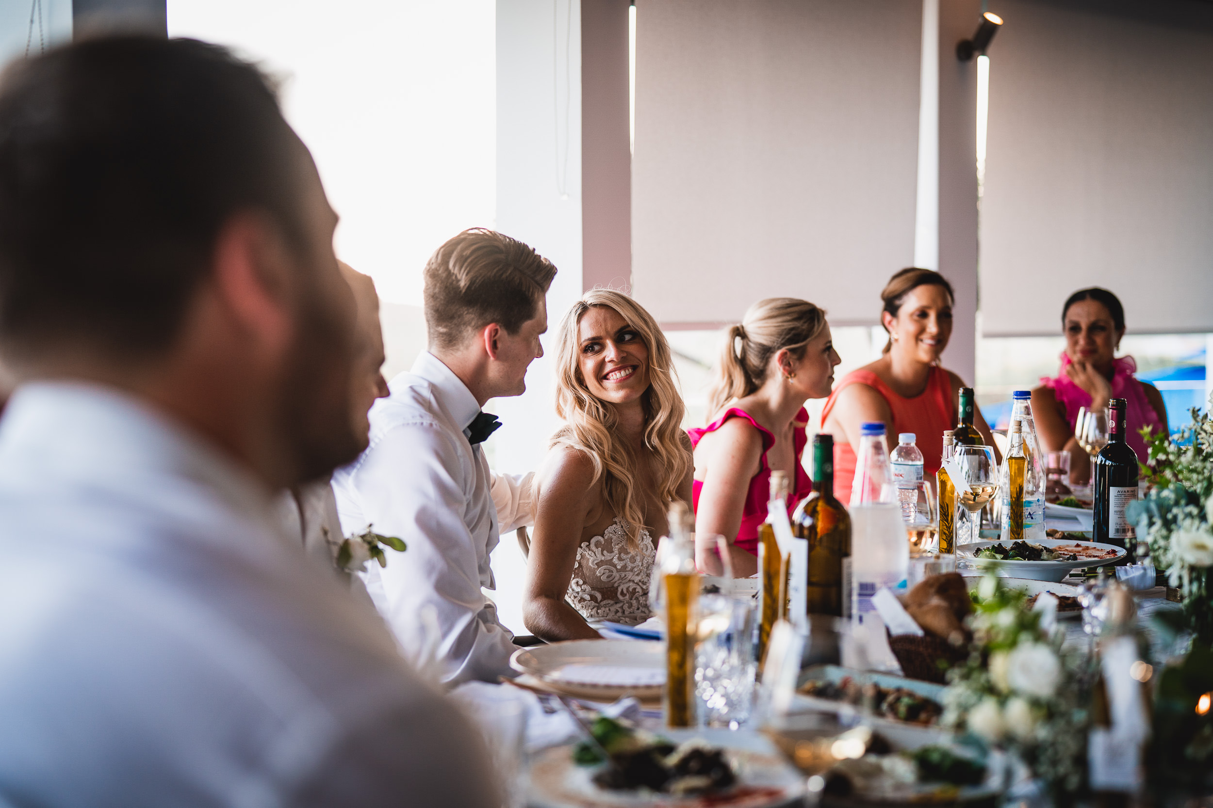 A group of people, including the bride and wedding photographer, sitting around a table at a wedding reception.
