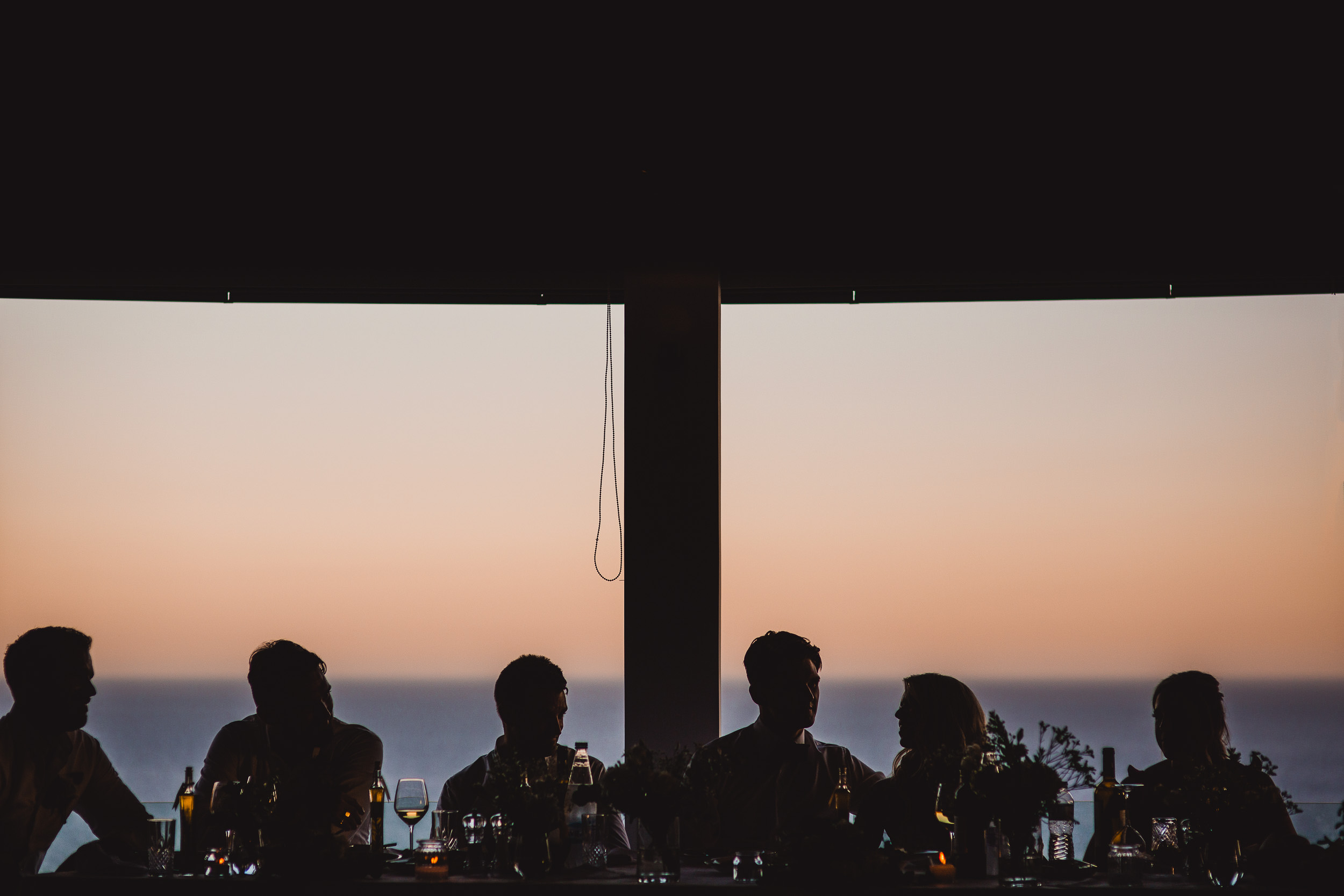 A bride and her wedding party seated at a table with a view of the ocean.