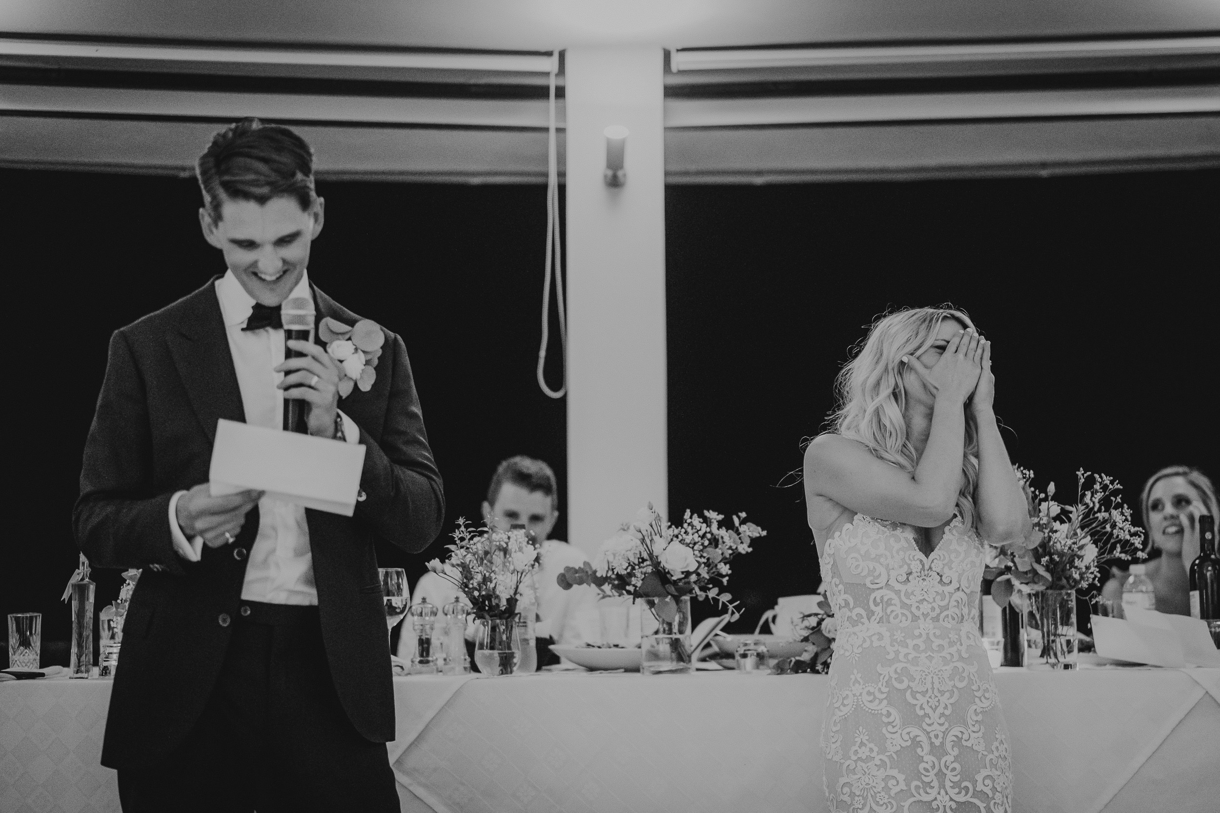A bride and groom joyfully sharing laughter during their wedding speech, captured by the wedding photographer.