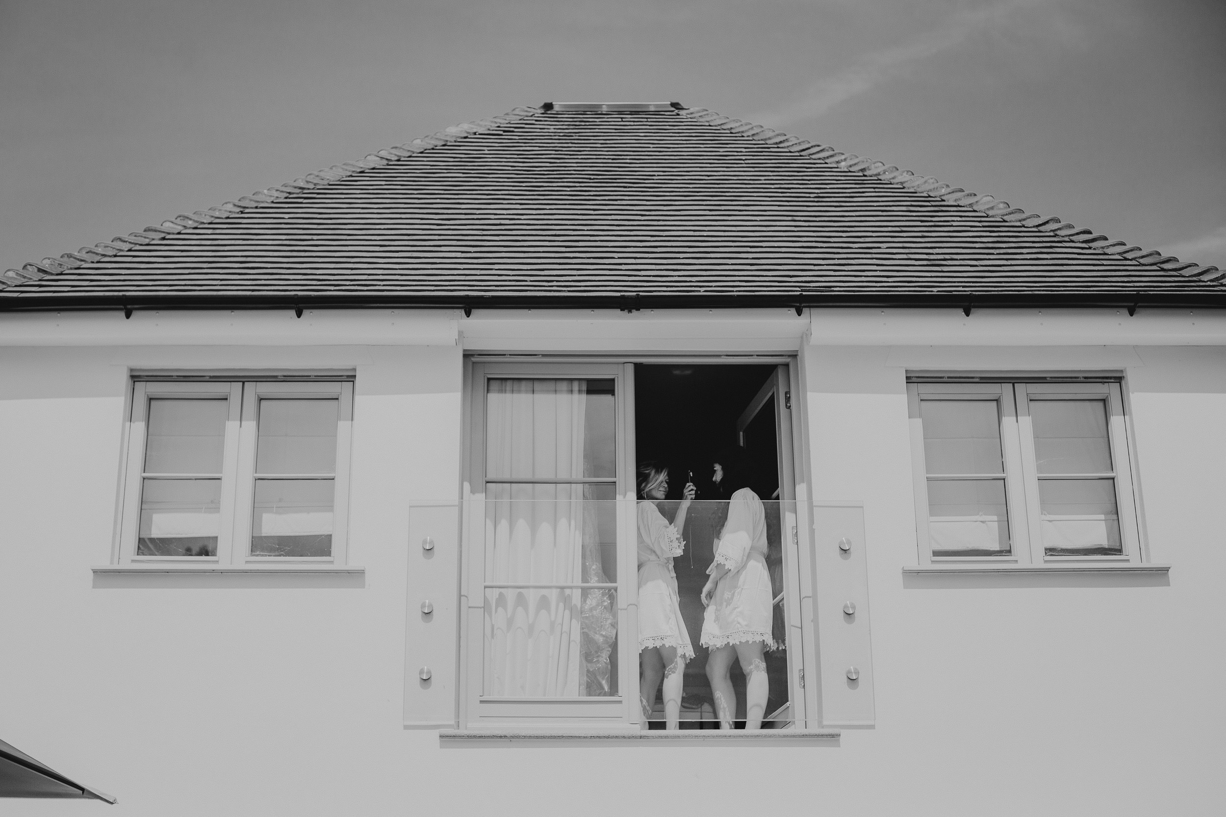 Black and white wedding photo of two women standing in the window of a house.