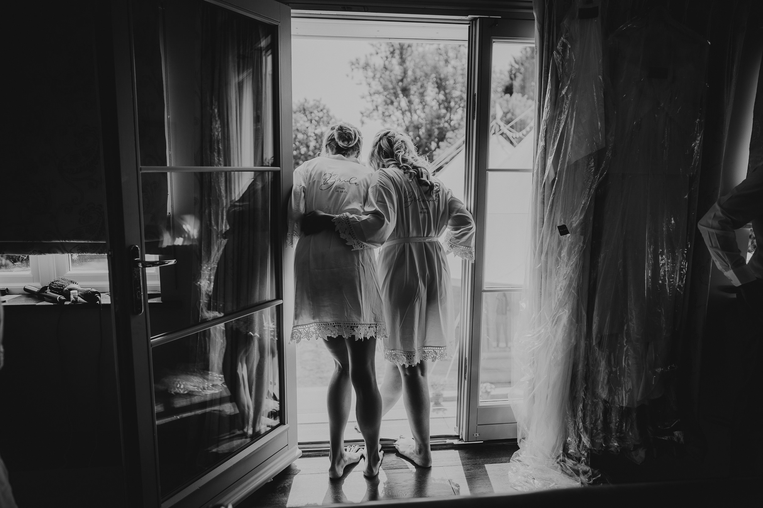 Two brides in robes standing in front of a door, captured by a wedding photographer.