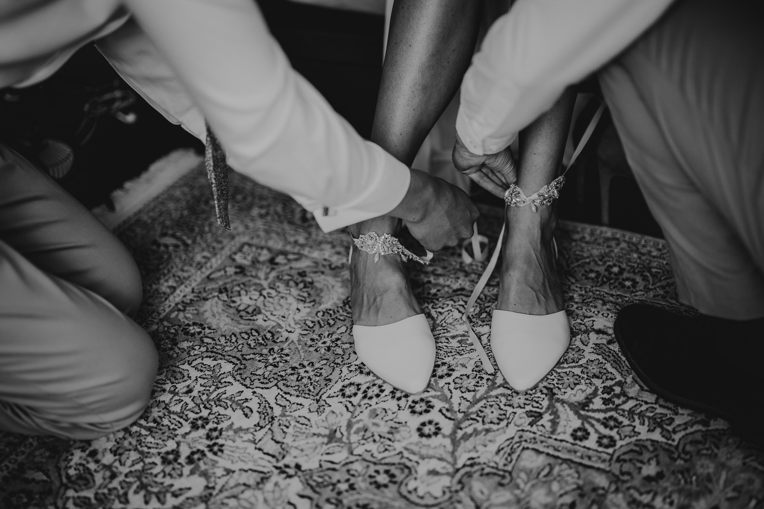 A wedding couple tying their shoes on a rug.