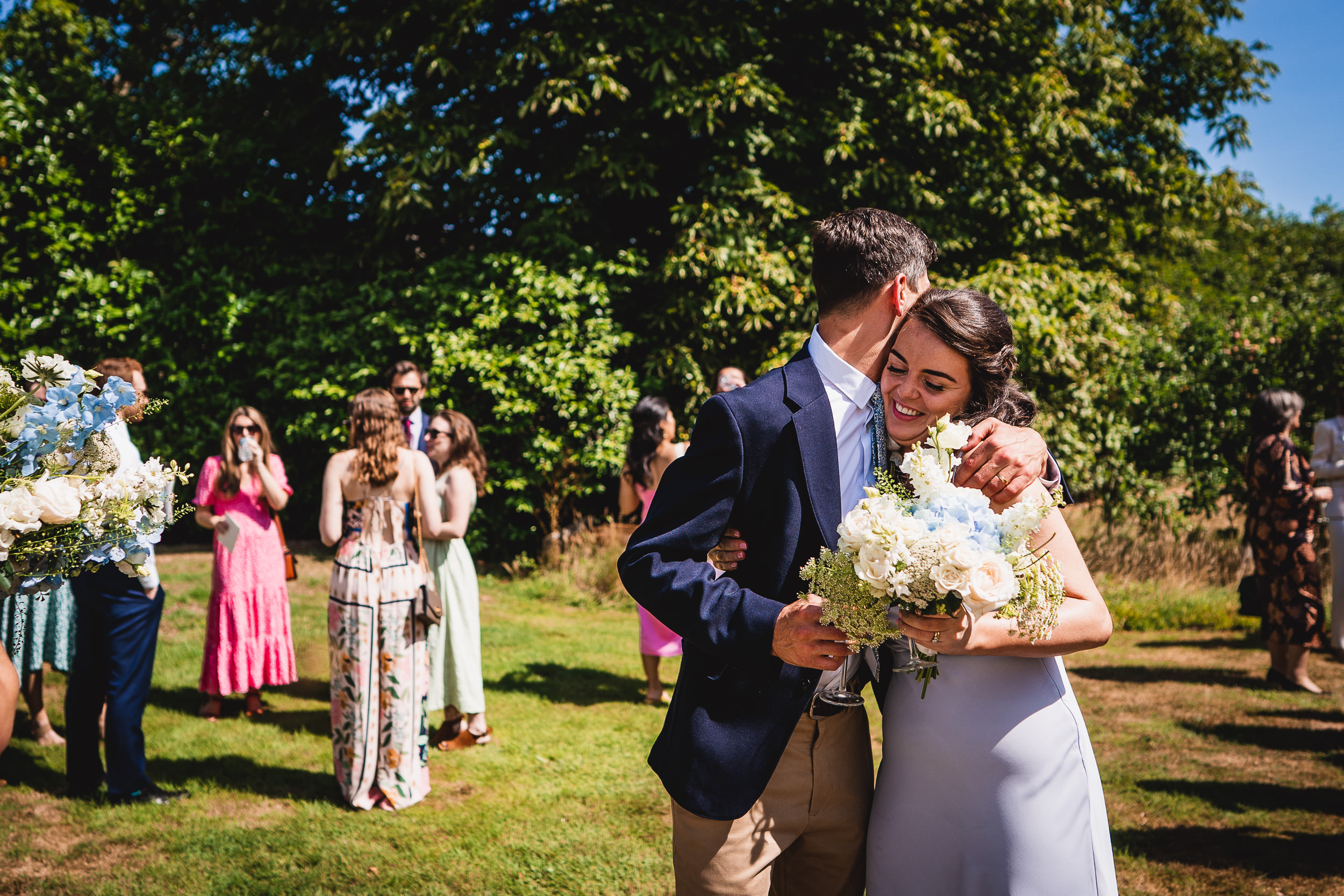 A wedding photographer capturing a bride and groom hugging among the crowd.