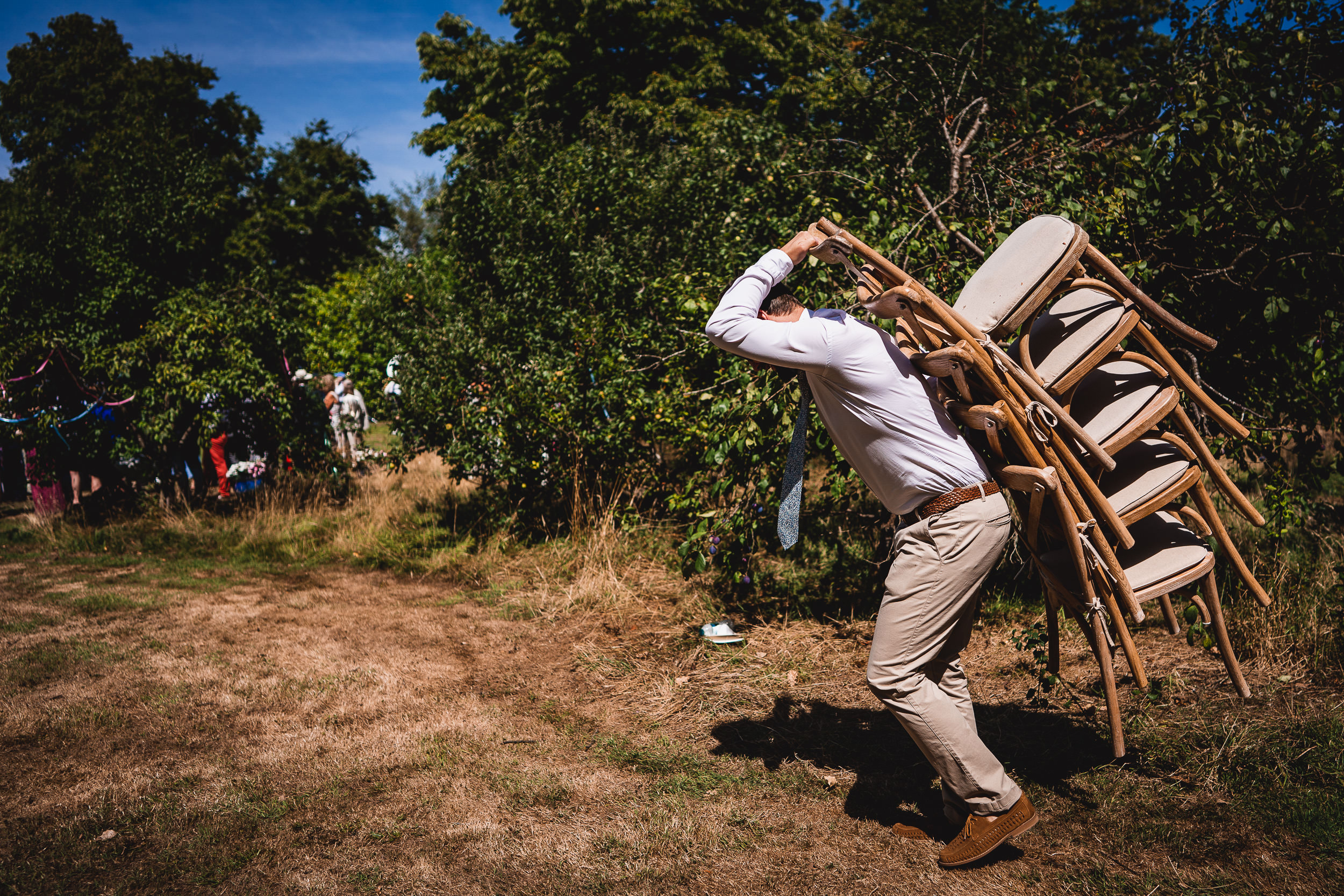 A groom being photographed with chairs in a field for his wedding.