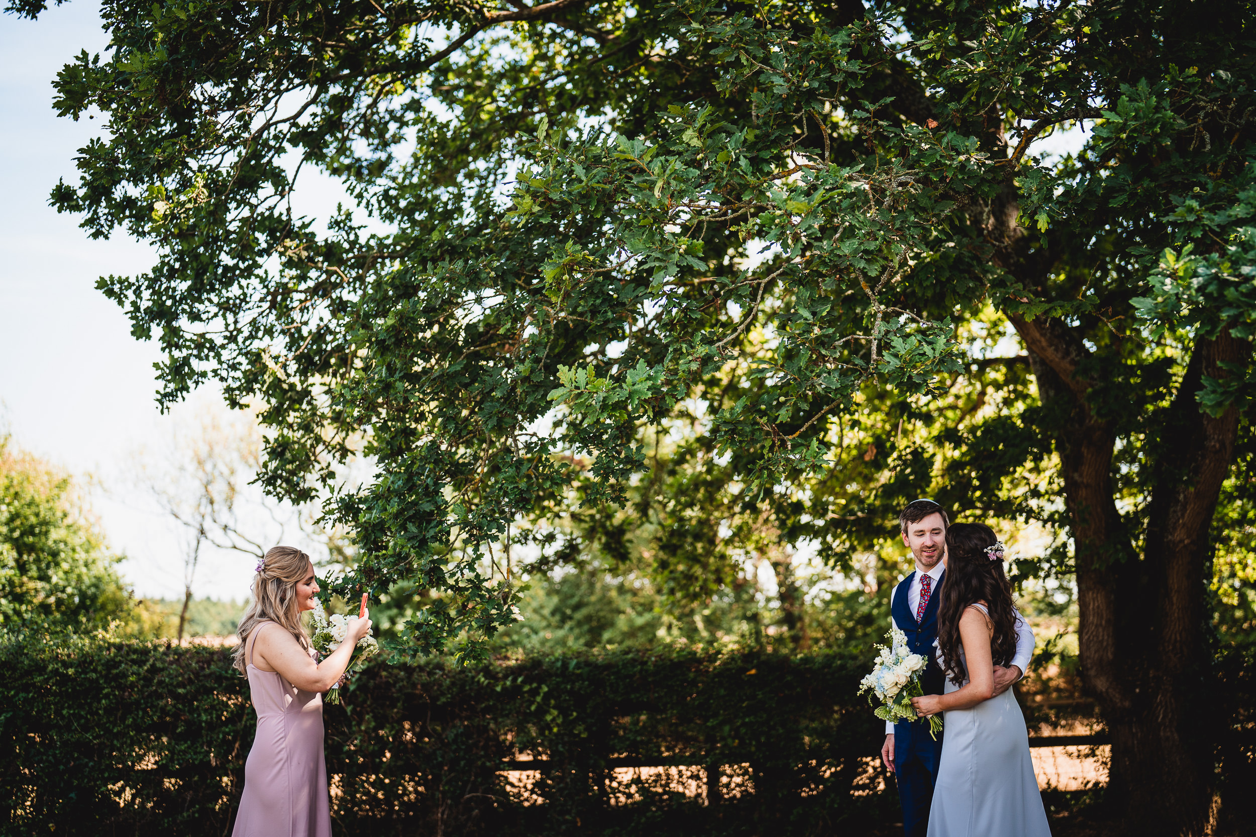 A bride and groom posing for their wedding photographer in front of a tree.