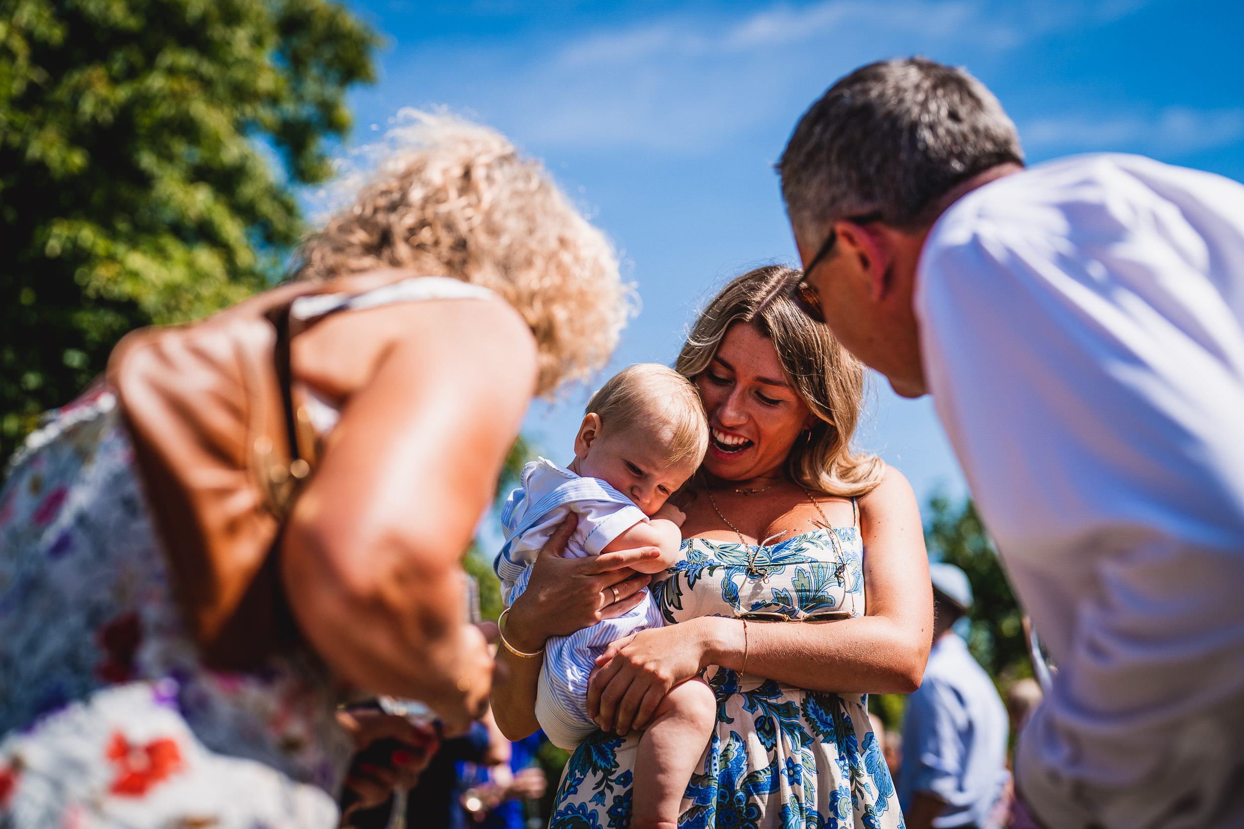 A bride holds a baby in her arms while the groom looks on.