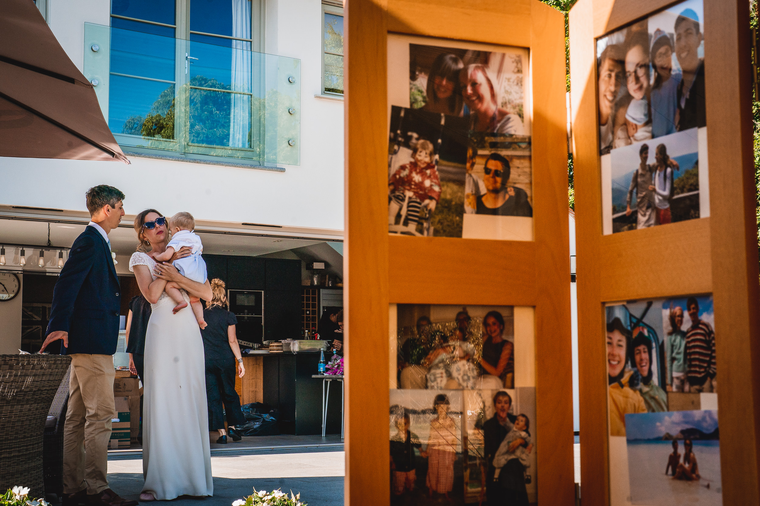 A bride, wedding photographer, and wedding party pose in front of a wooden frame adorned with pictures.