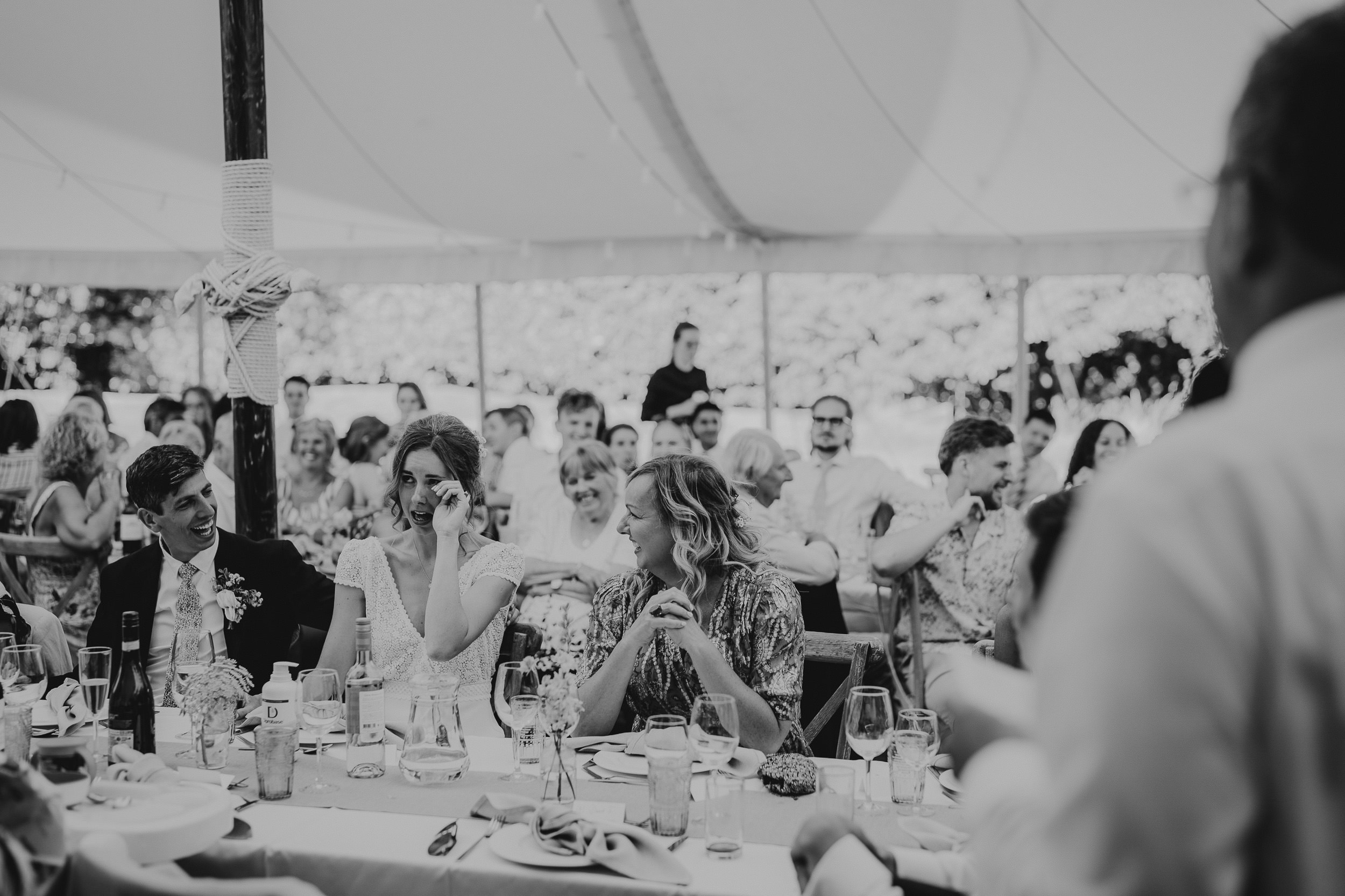 A black and white photo capturing a wedding reception in a tent, taken by a wedding photographer.