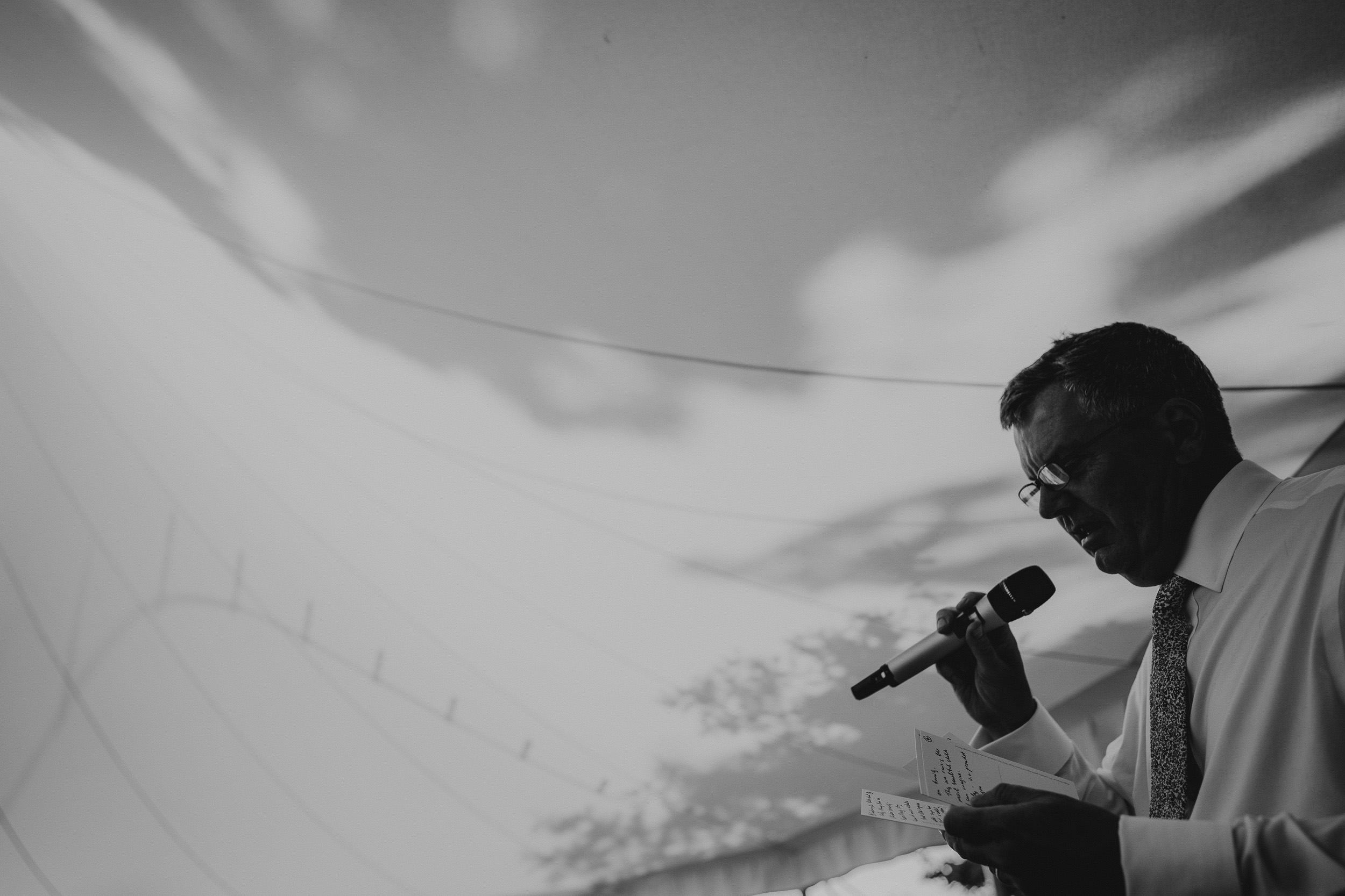 A photographer capturing the bride's speech at a wedding, using a microphone under a tent.