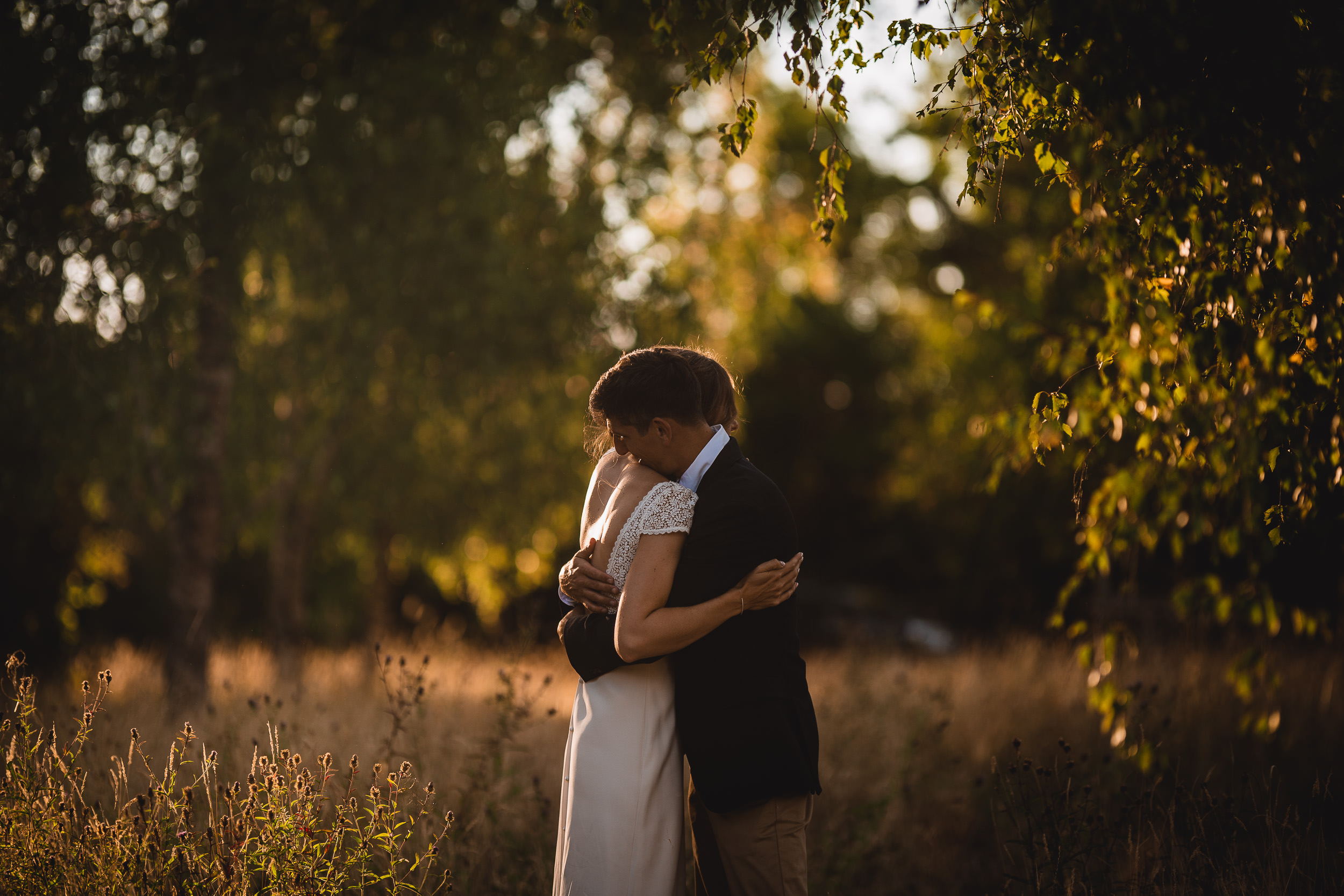 A bride and groom embracing during their sunset wedding photoshoot in a picturesque field.