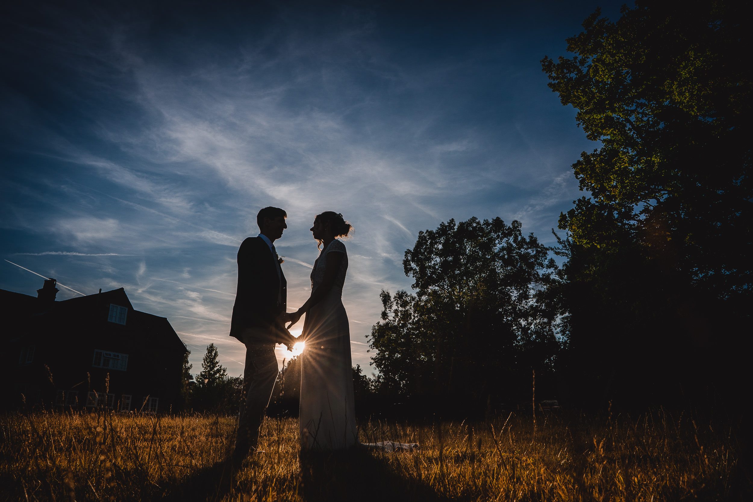 A bride and groom captured by a wedding photographer in a field at sunset.