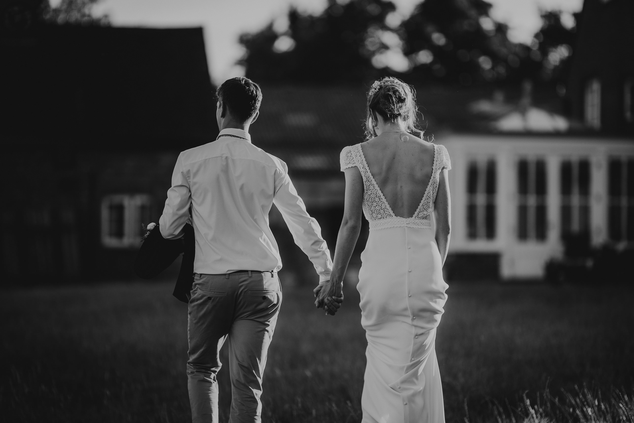 Black and white wedding photo of bride and groom walking in a field.