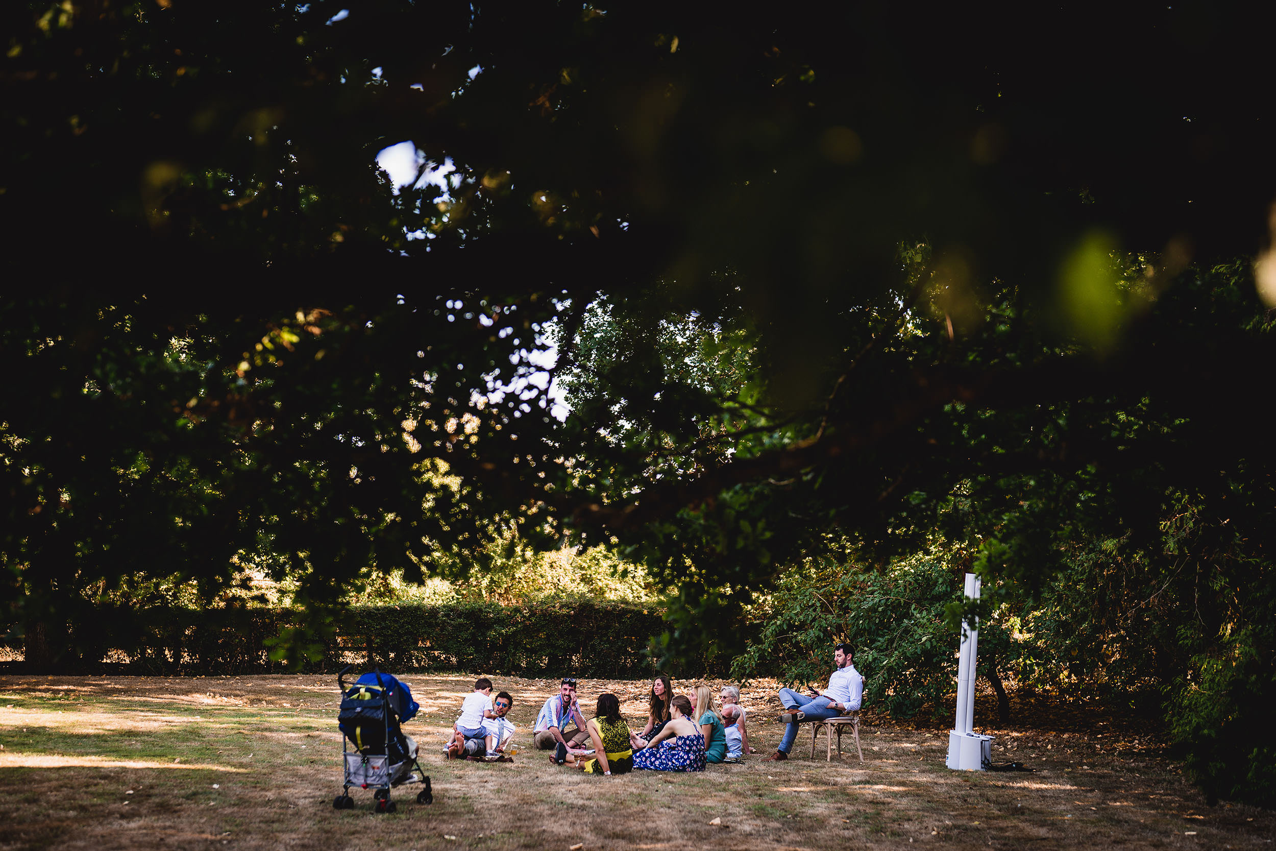 A wedding photographer captures the groom and bride sitting under a tree.