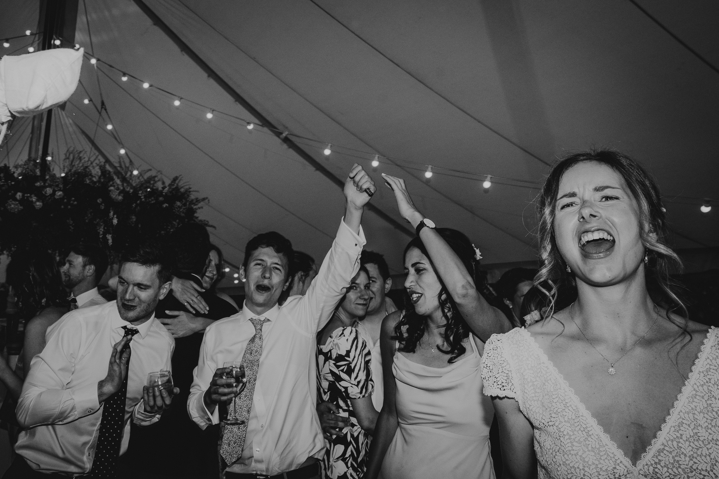 A black and white wedding photo capturing a group of people dancing in a tent.