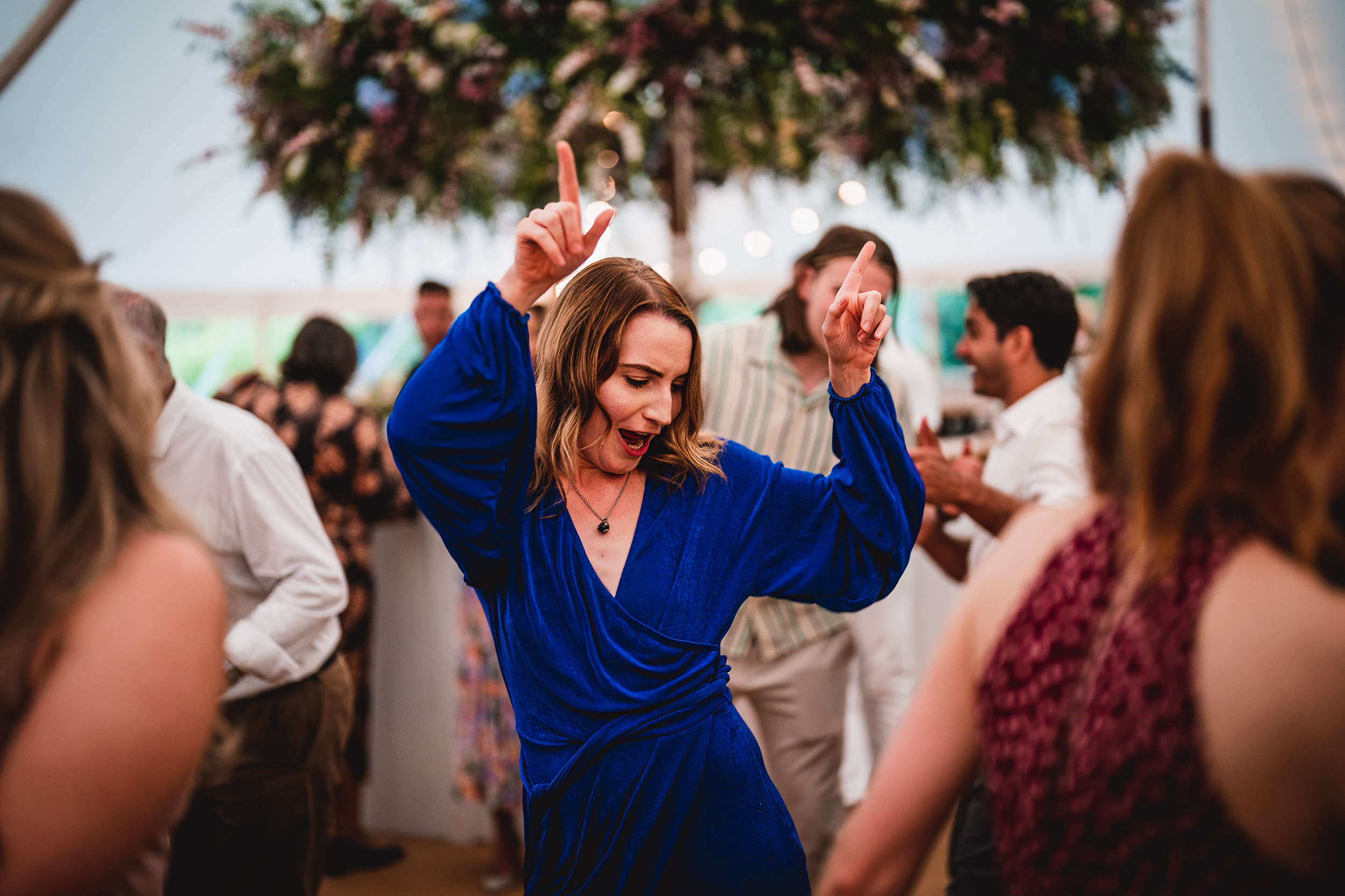A wedding photographer captures a woman dancing at a wedding in a tent.